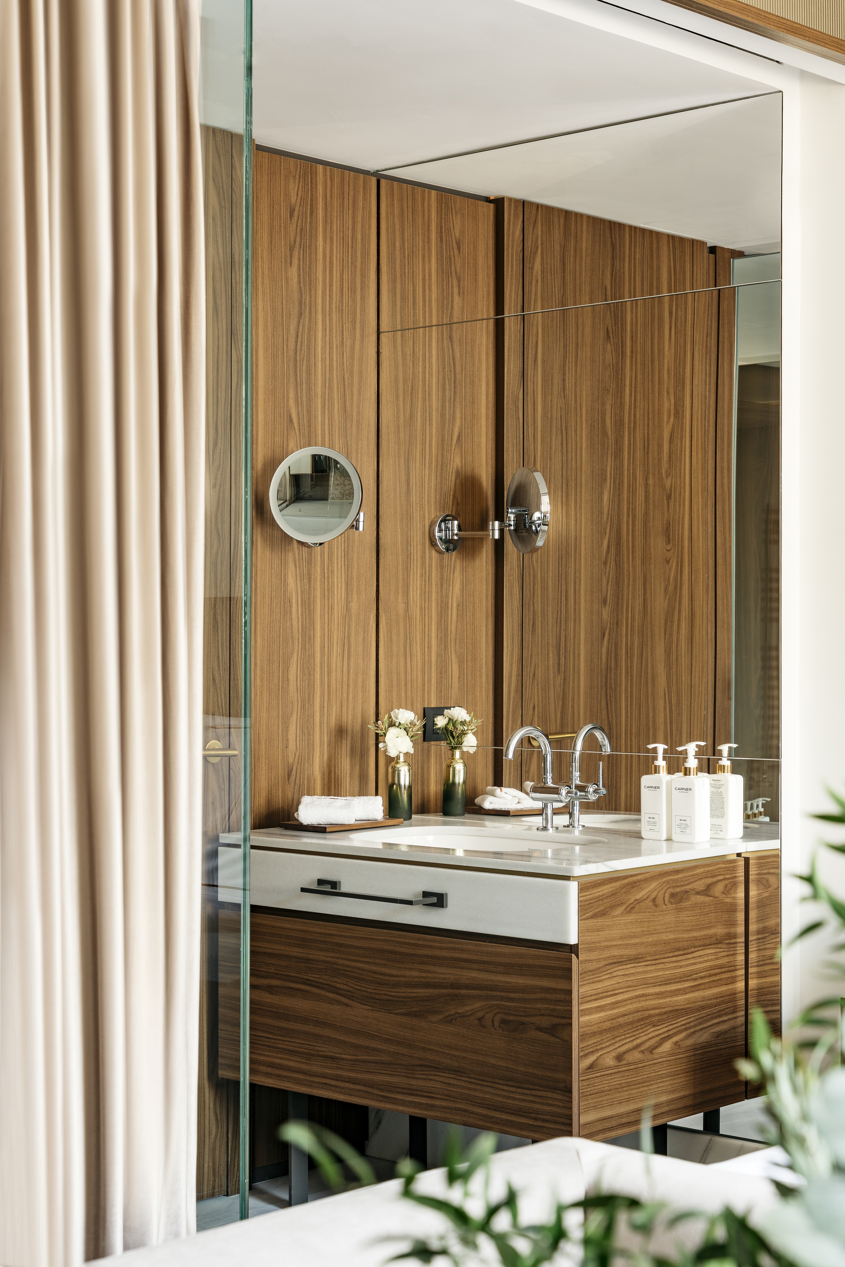 Modern wood bathroom vanity with marble counter, chrome faucets, and toiletries.