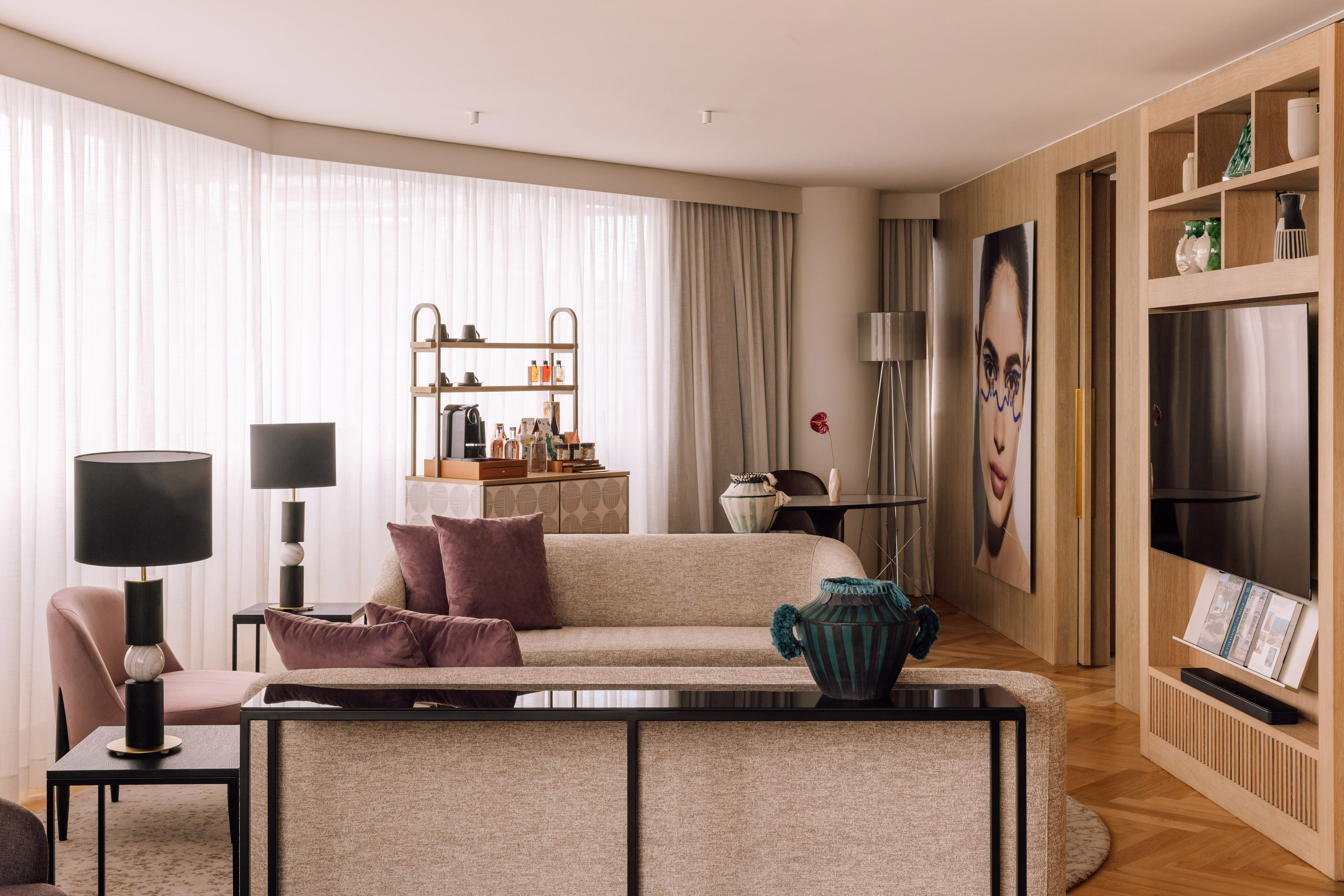 Modern hotel suite living room with beige sofa, wood accents, and contemporary art.
