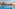 Sunny resort pool, palm trees, elephant statues, and red hotel buildings.