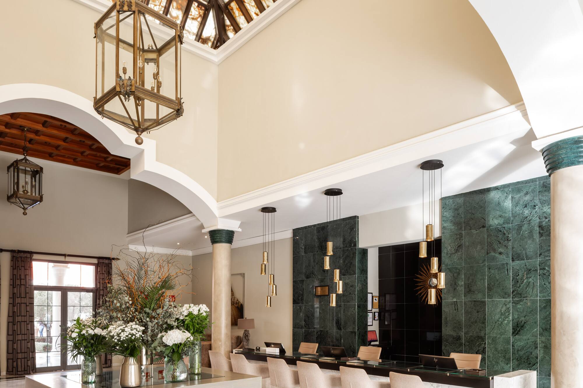 Grand hotel lobby with ornate skylight, marble floor, chandelier, and reception desk.