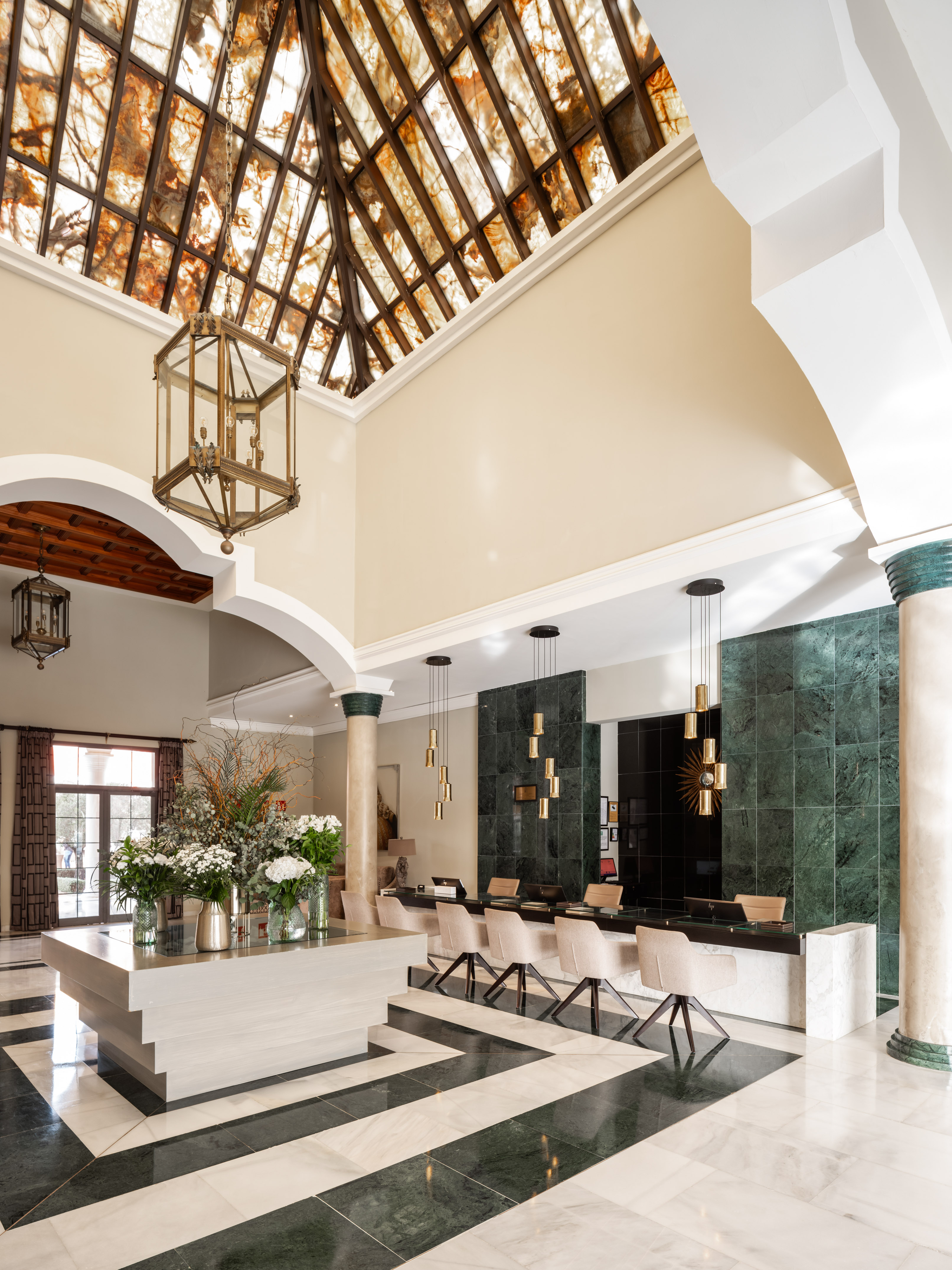 Grand hotel lobby with ornate skylight, marble floor, chandelier, and reception desk.