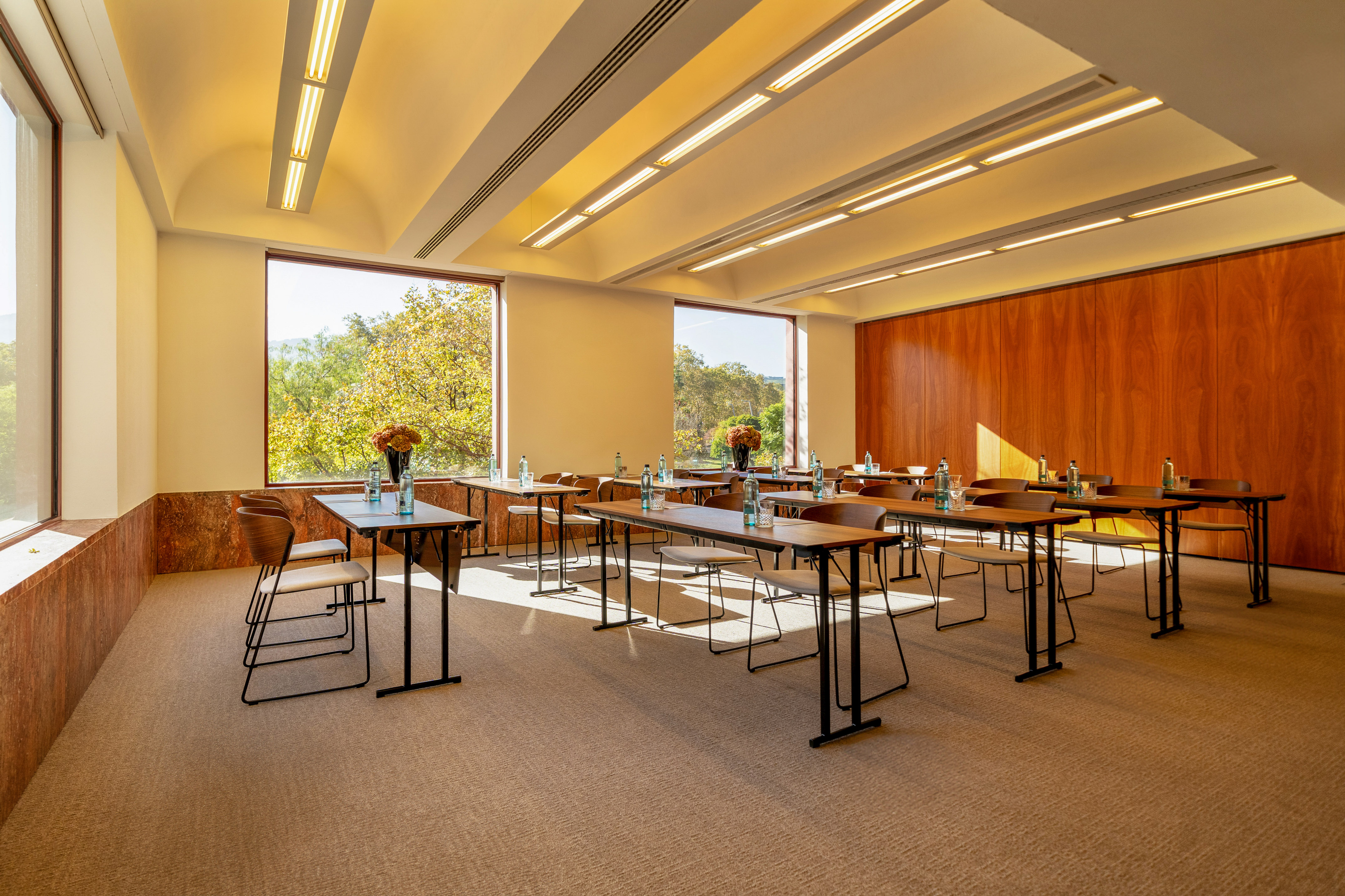 Bright conference room with classroom setup, large windows, and wood paneling.
