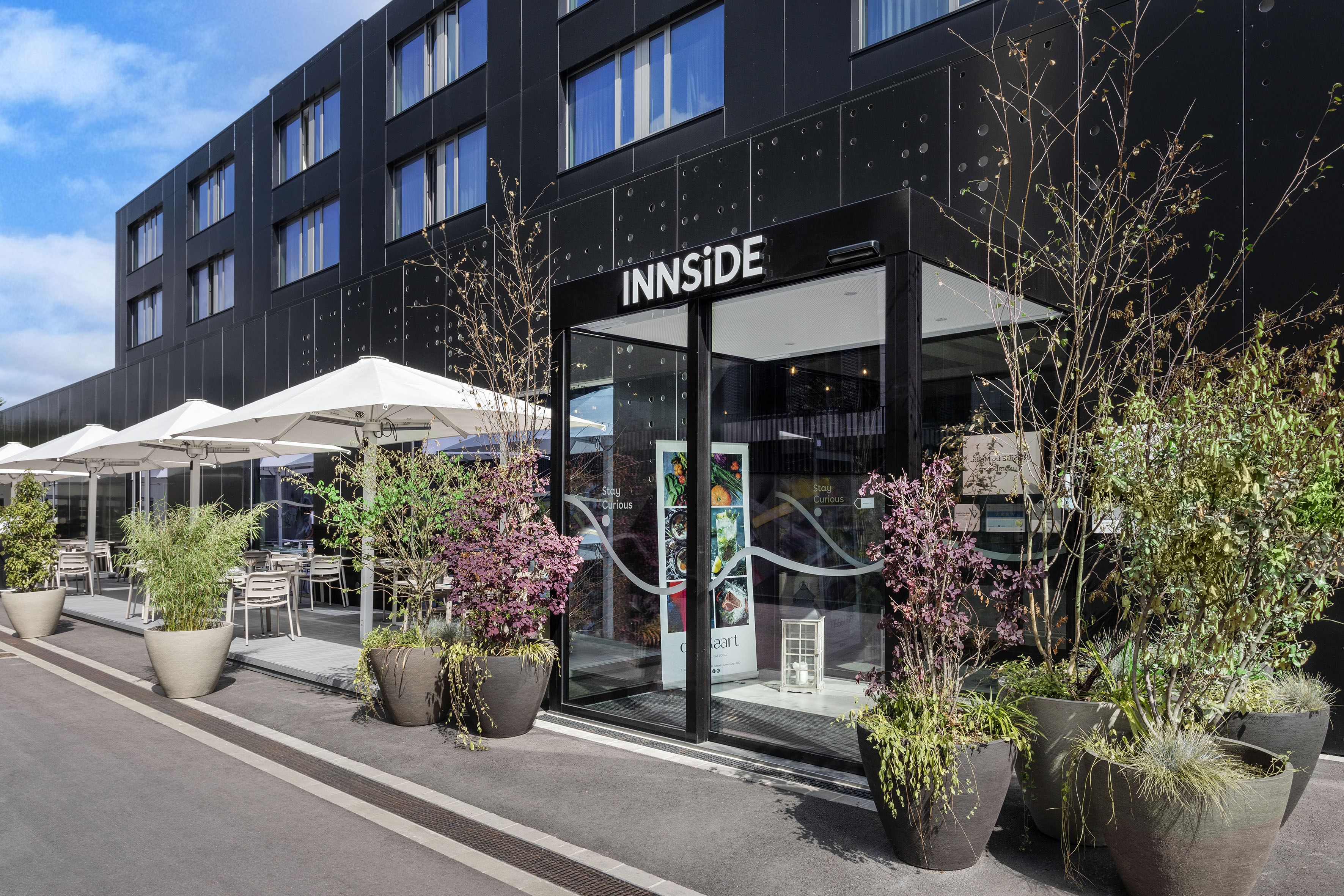 INNSIDE hotel exterior with modern black building, outdoor patio, and potted plants.