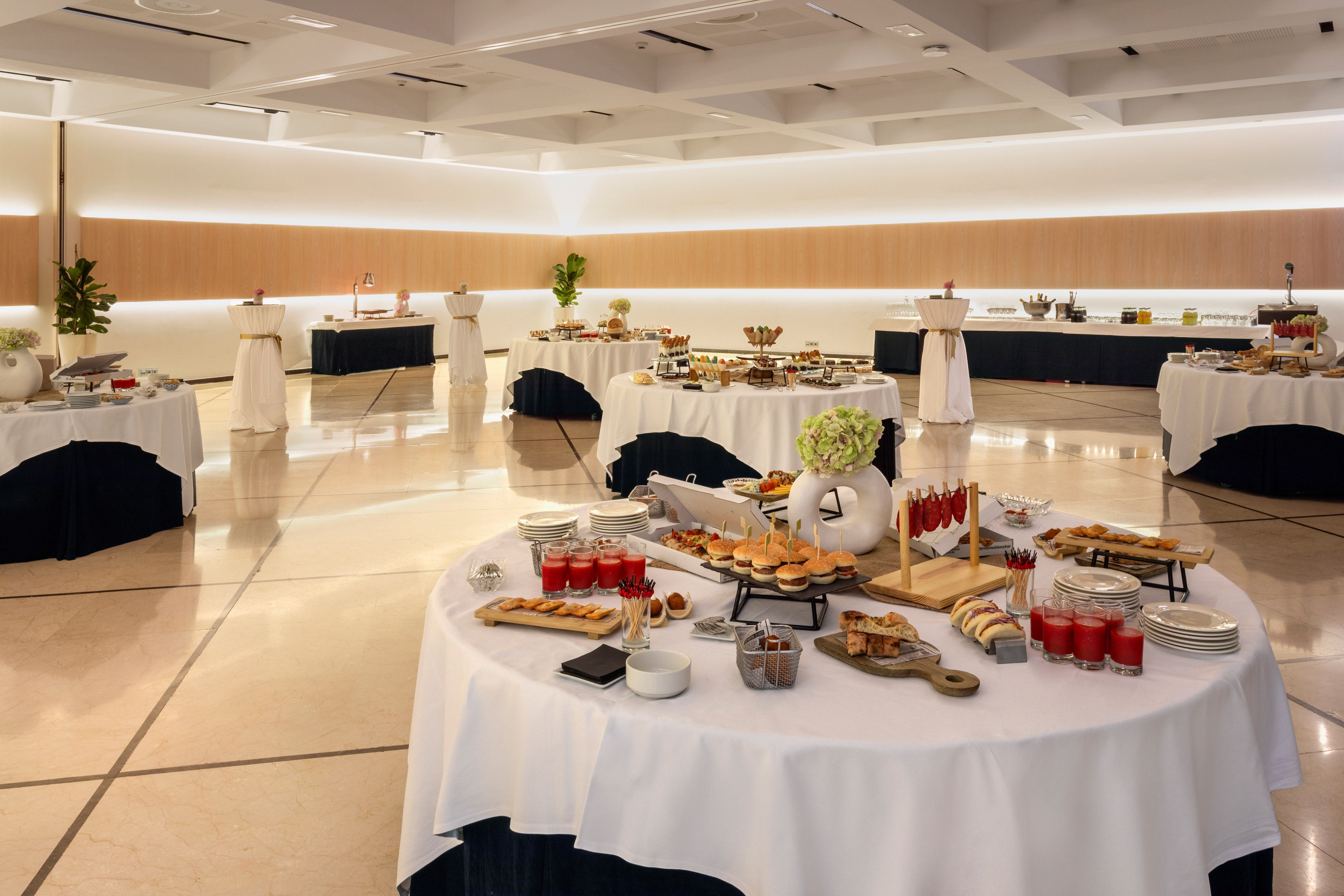 Buffet catering in a modern event hall with appetizers, sliders, and drinks.