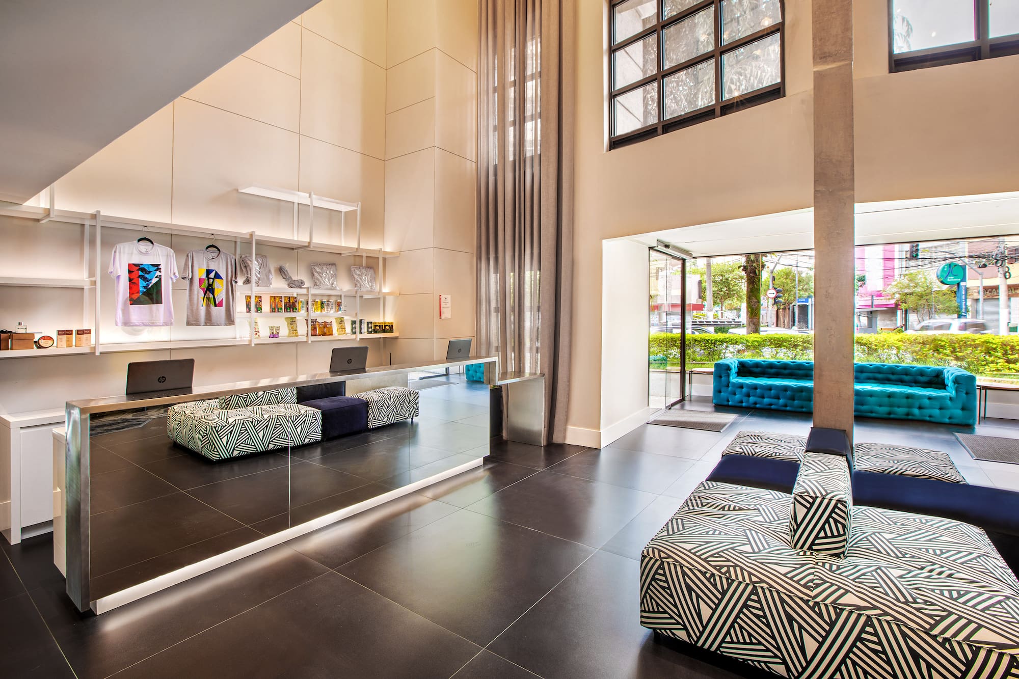 Stylish hotel lobby: mirrored desk, retail display, geometric benches, and turquoise sofas.