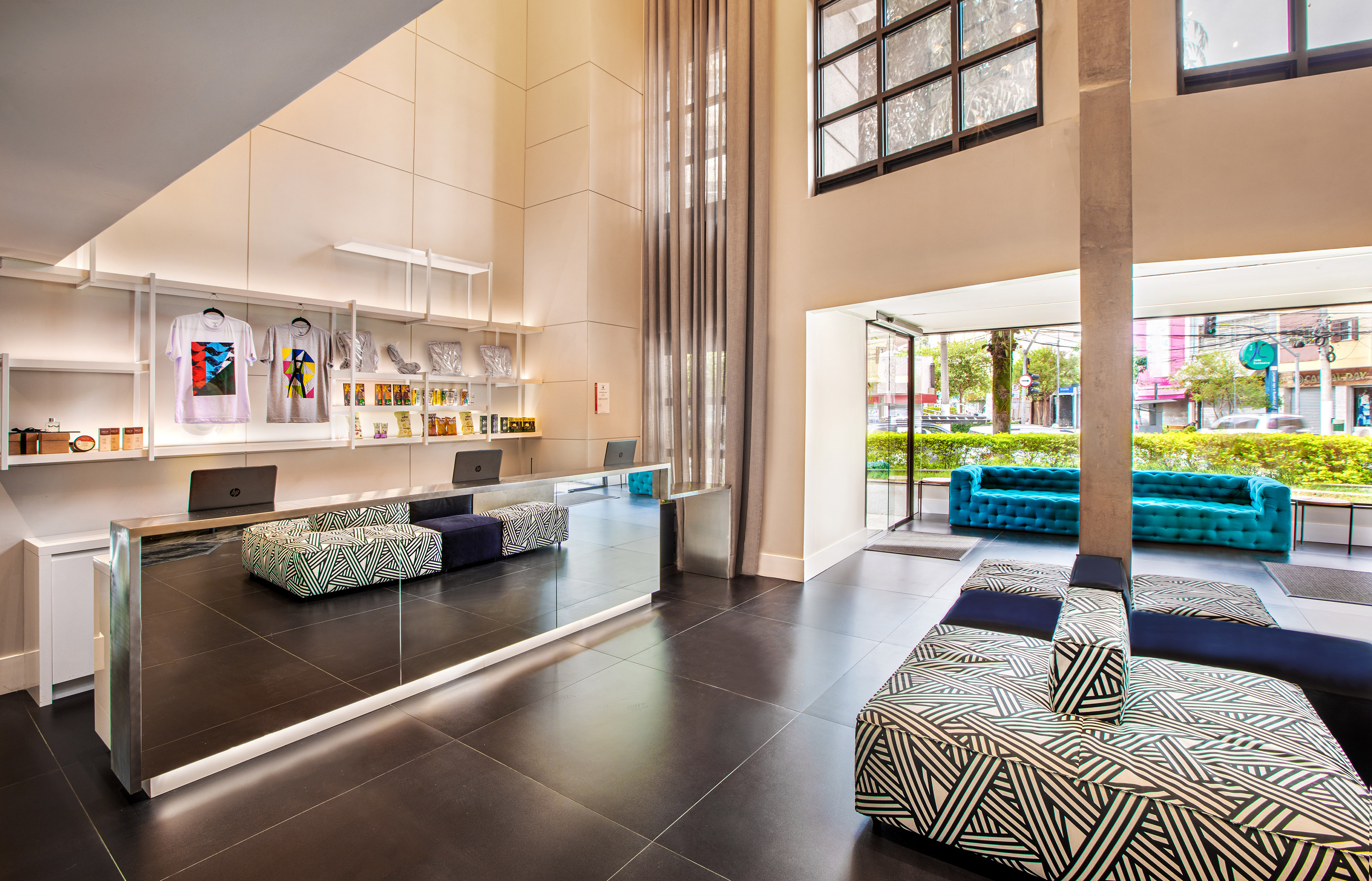 Stylish hotel lobby: mirrored desk, retail display, geometric benches, and turquoise sofas.