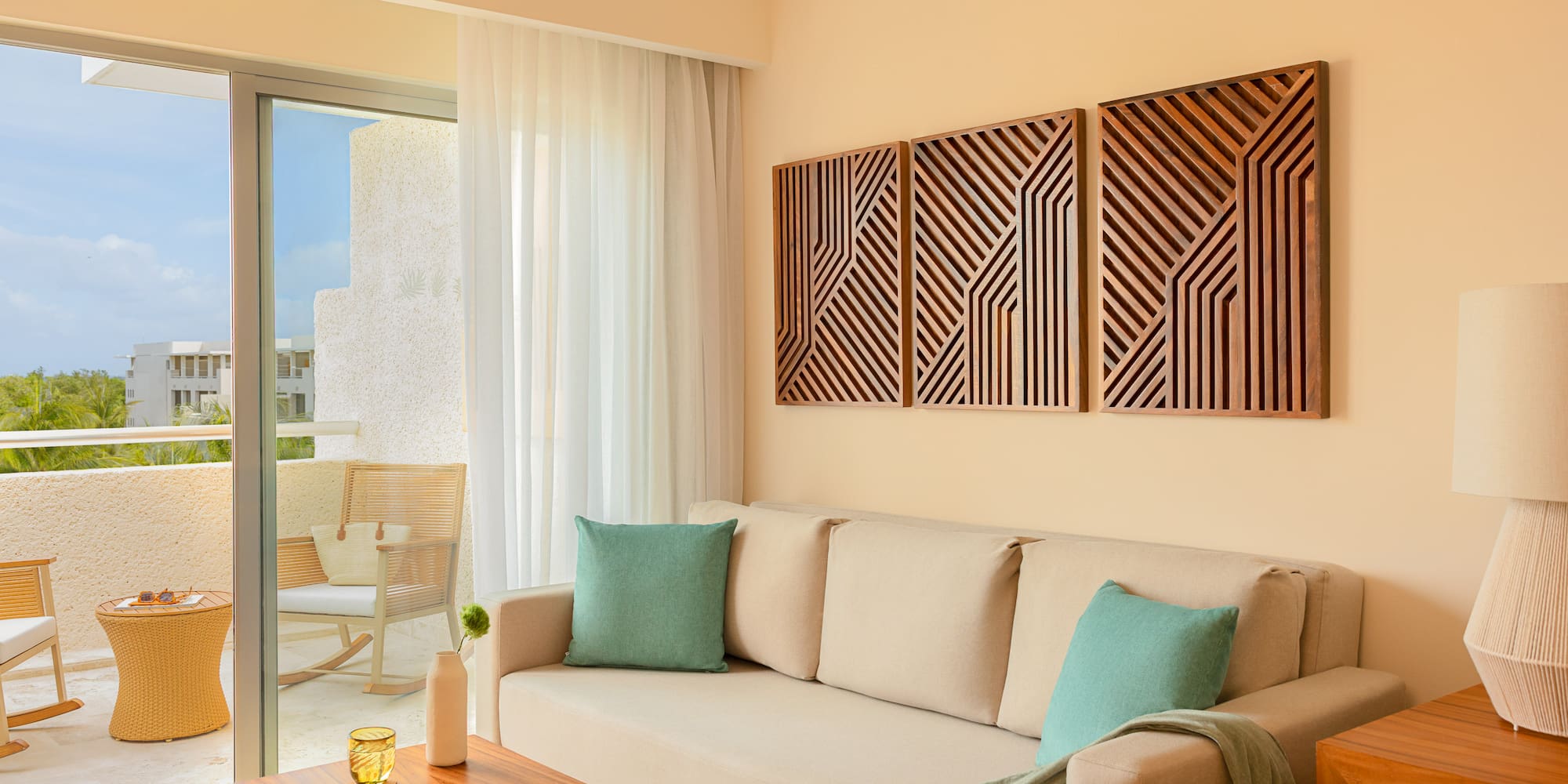 Hotel living room: beige sofa, geometric wood art, tropical balcony.