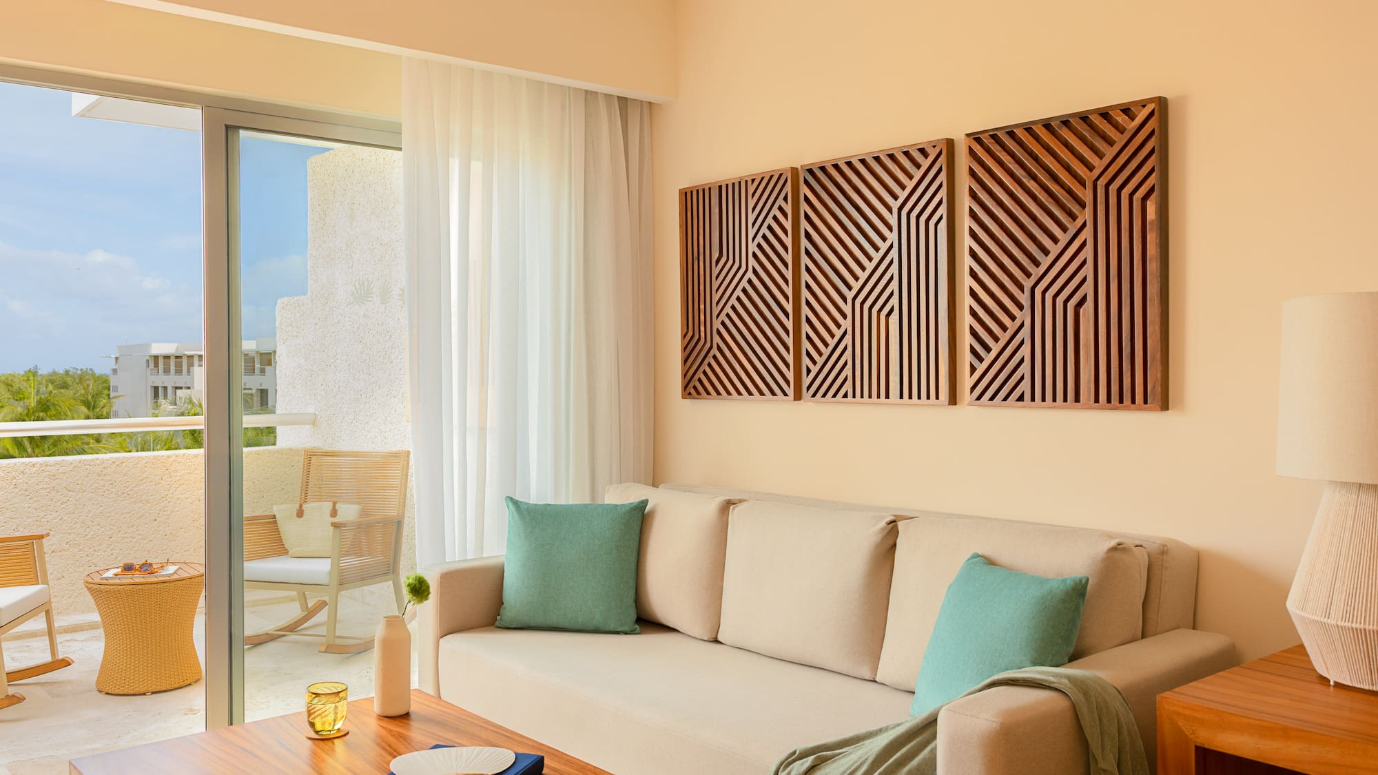Hotel living room: beige sofa, geometric wood art, tropical balcony.