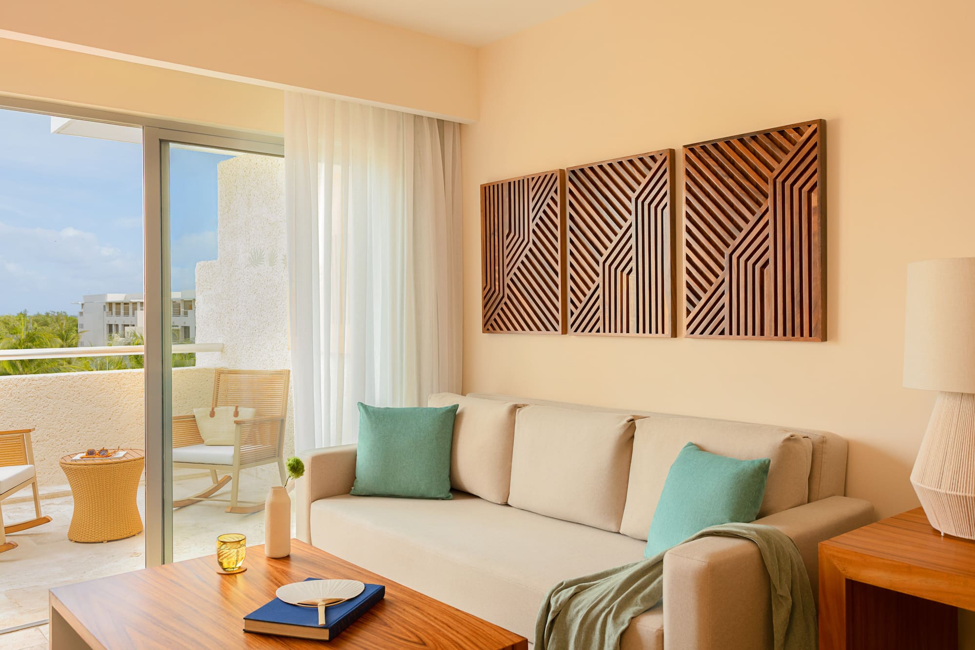Hotel living room: beige sofa, geometric wood art, tropical balcony.
