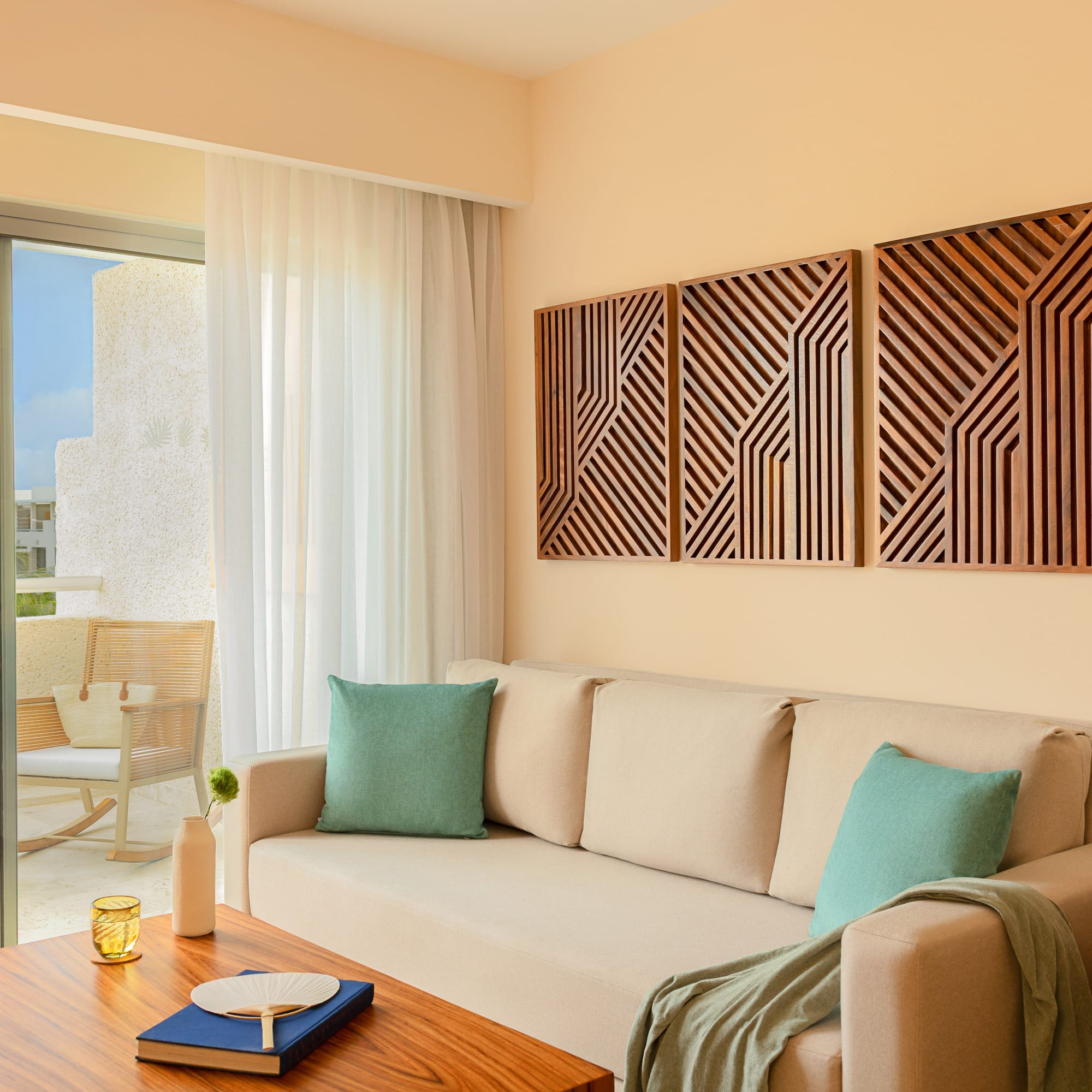 Hotel living room: beige sofa, geometric wood art, tropical balcony.