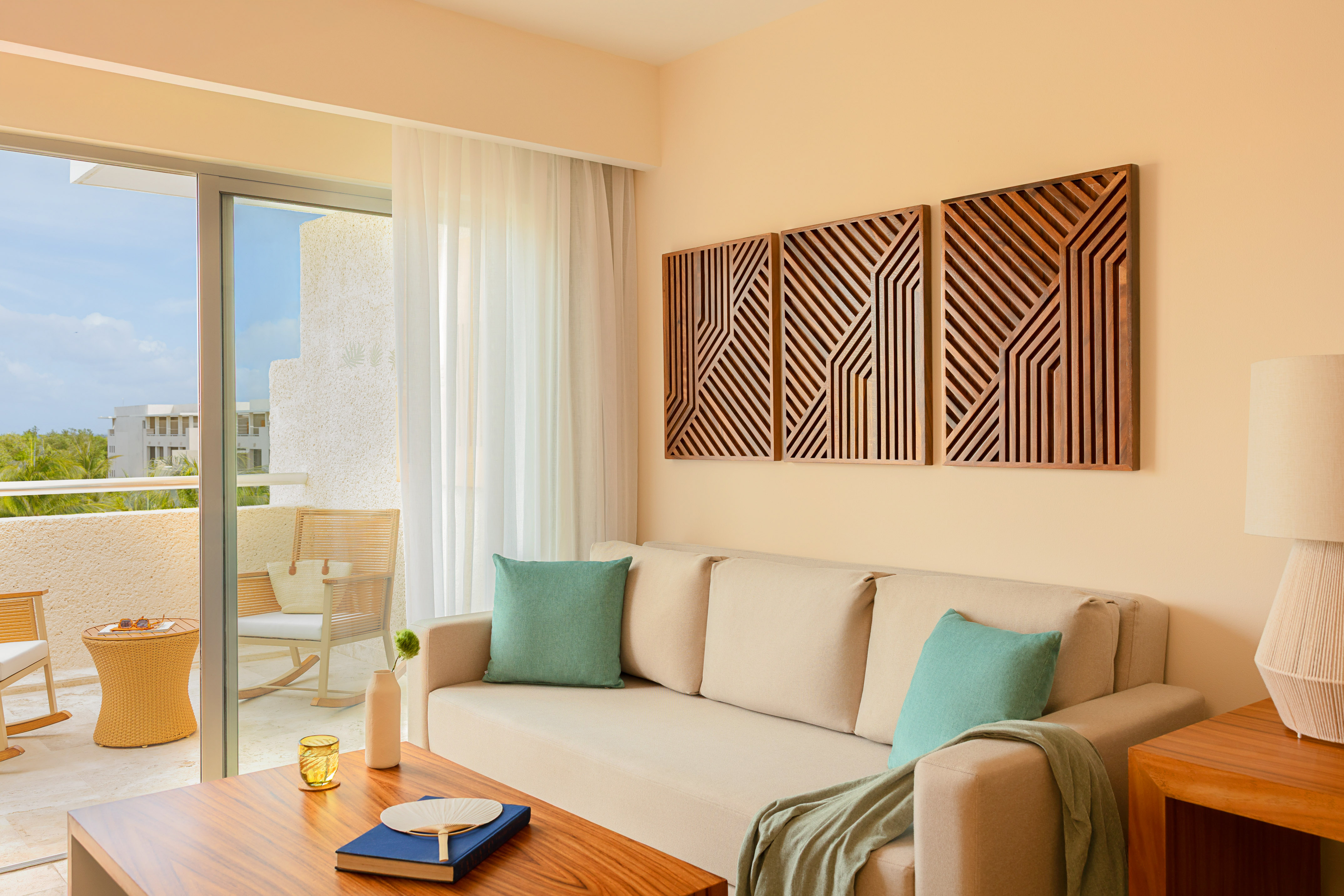Hotel living room: beige sofa, geometric wood art, tropical balcony.