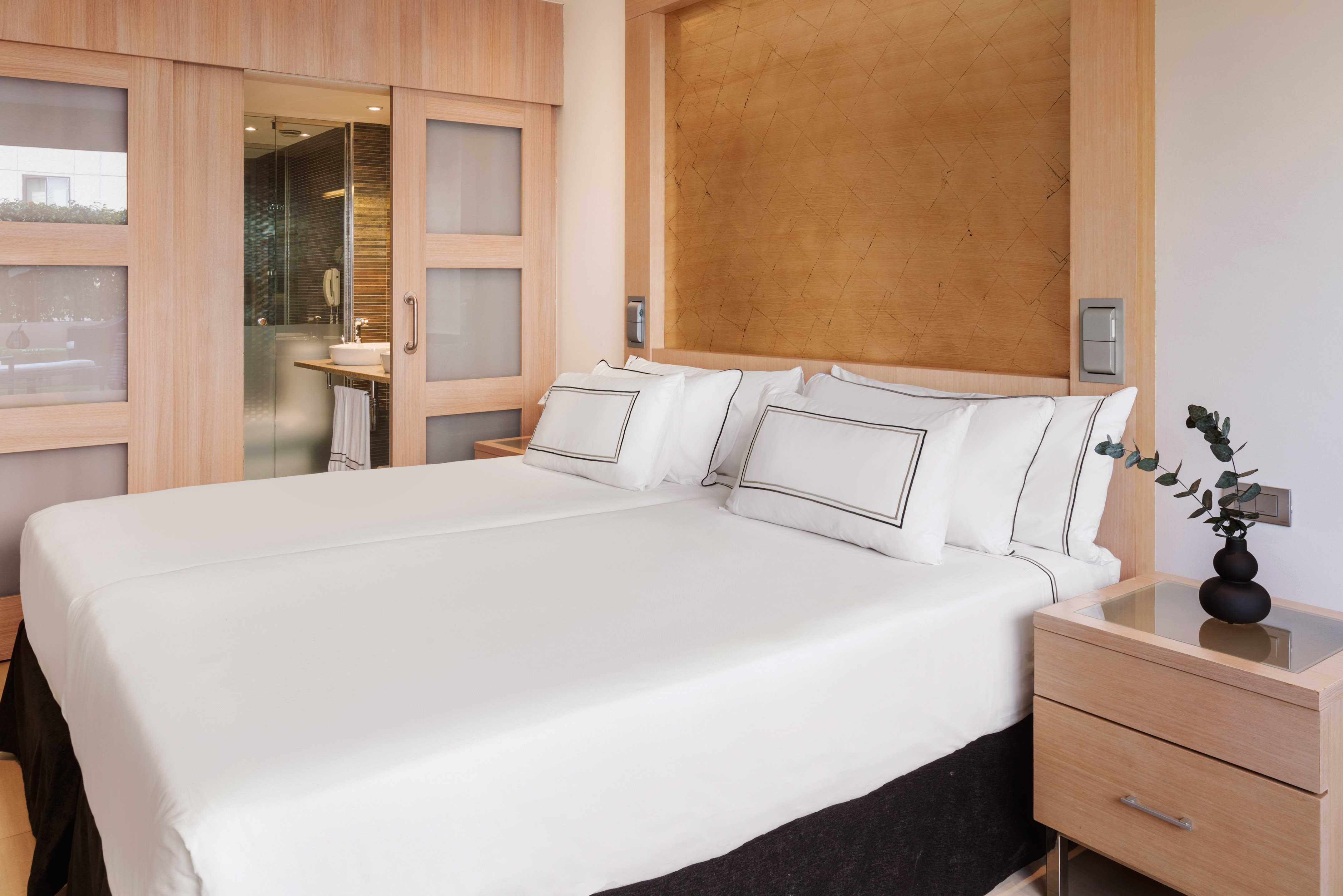 Modern hotel bedroom with twin beds, wooden decor, and sliding bathroom door.