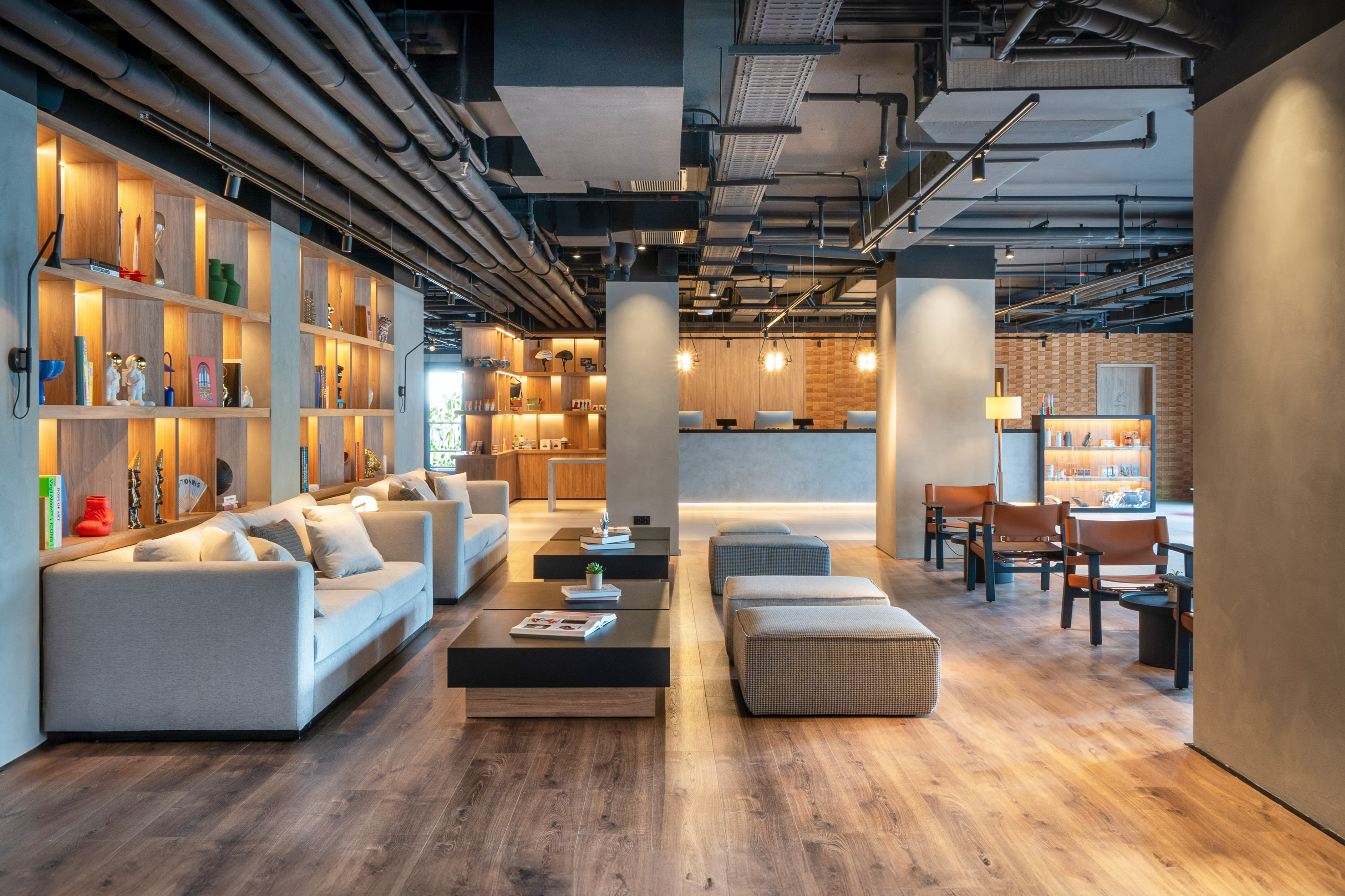 Modern hotel lobby lounge with grey sofas, industrial ceiling, and reception desk.