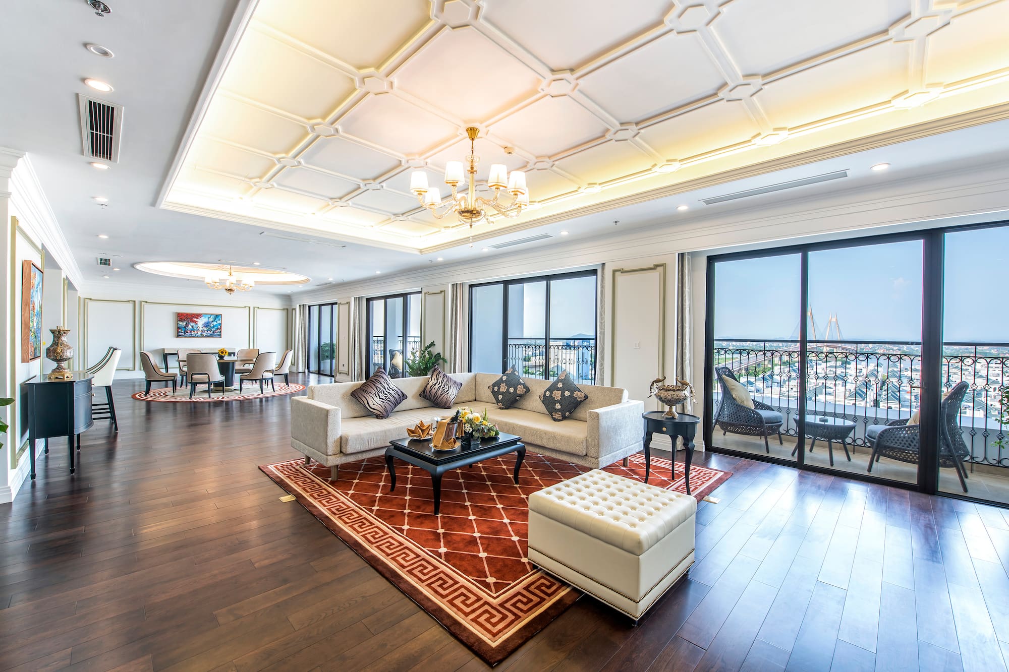 Spacious luxury living room with city view balcony, sectional sofa, and dark wood floor.