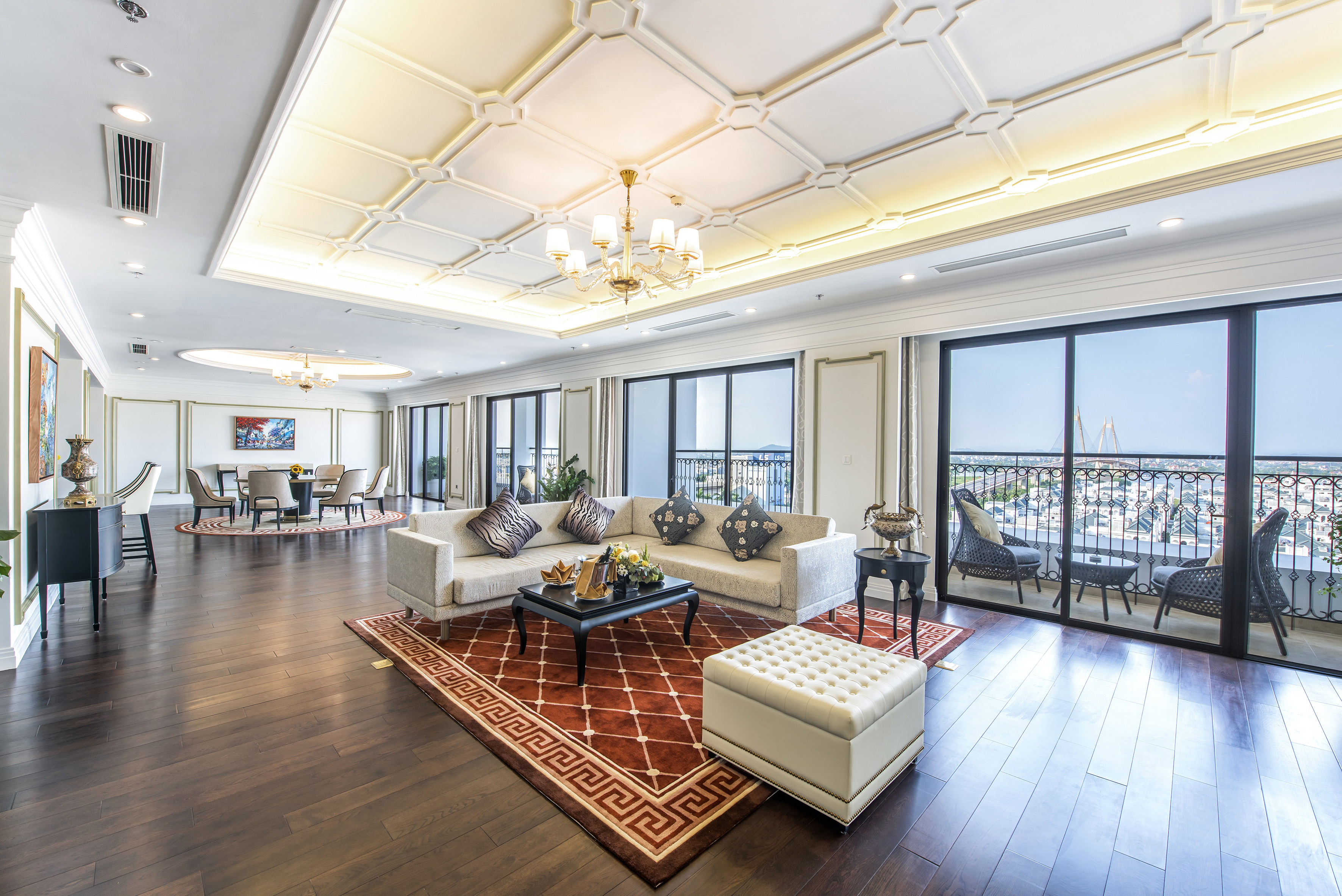 Spacious luxury living room with city view balcony, sectional sofa, and dark wood floor.
