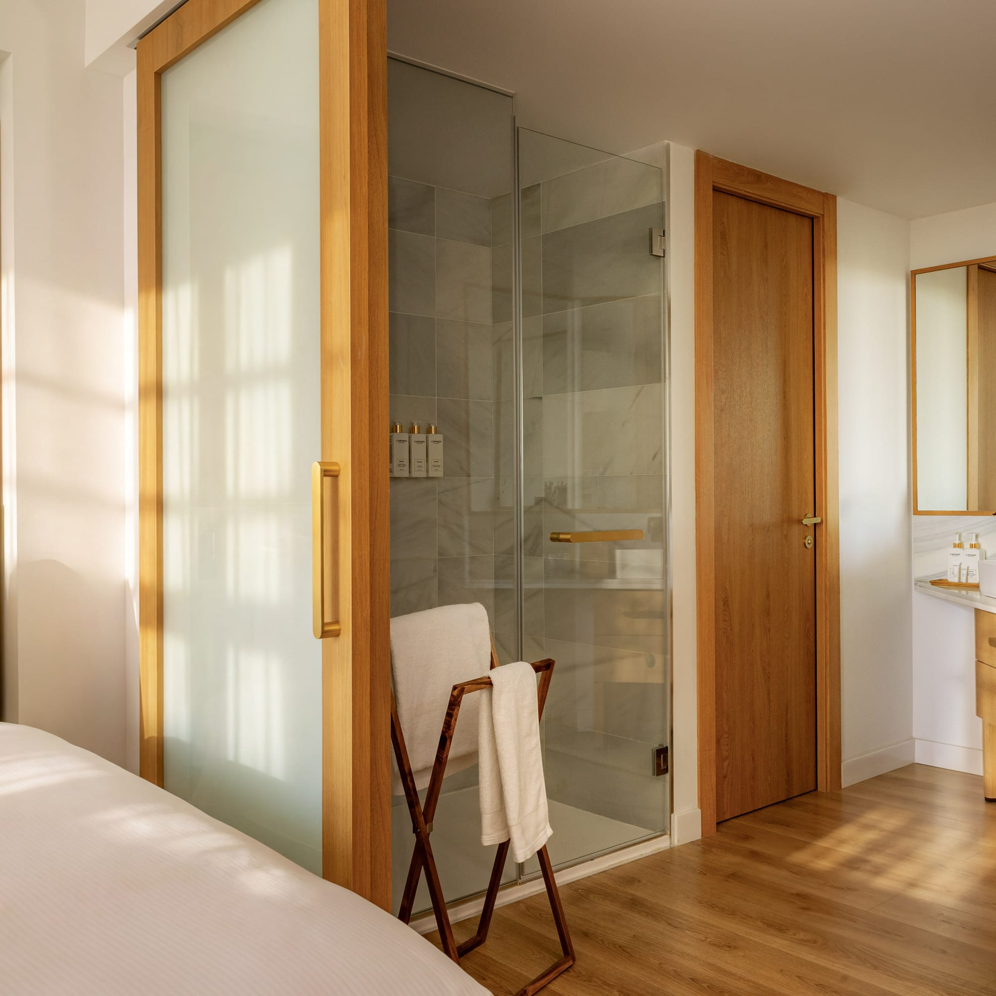 Modern hotel room: bed, sliding door to bathroom with glass shower & vanity.