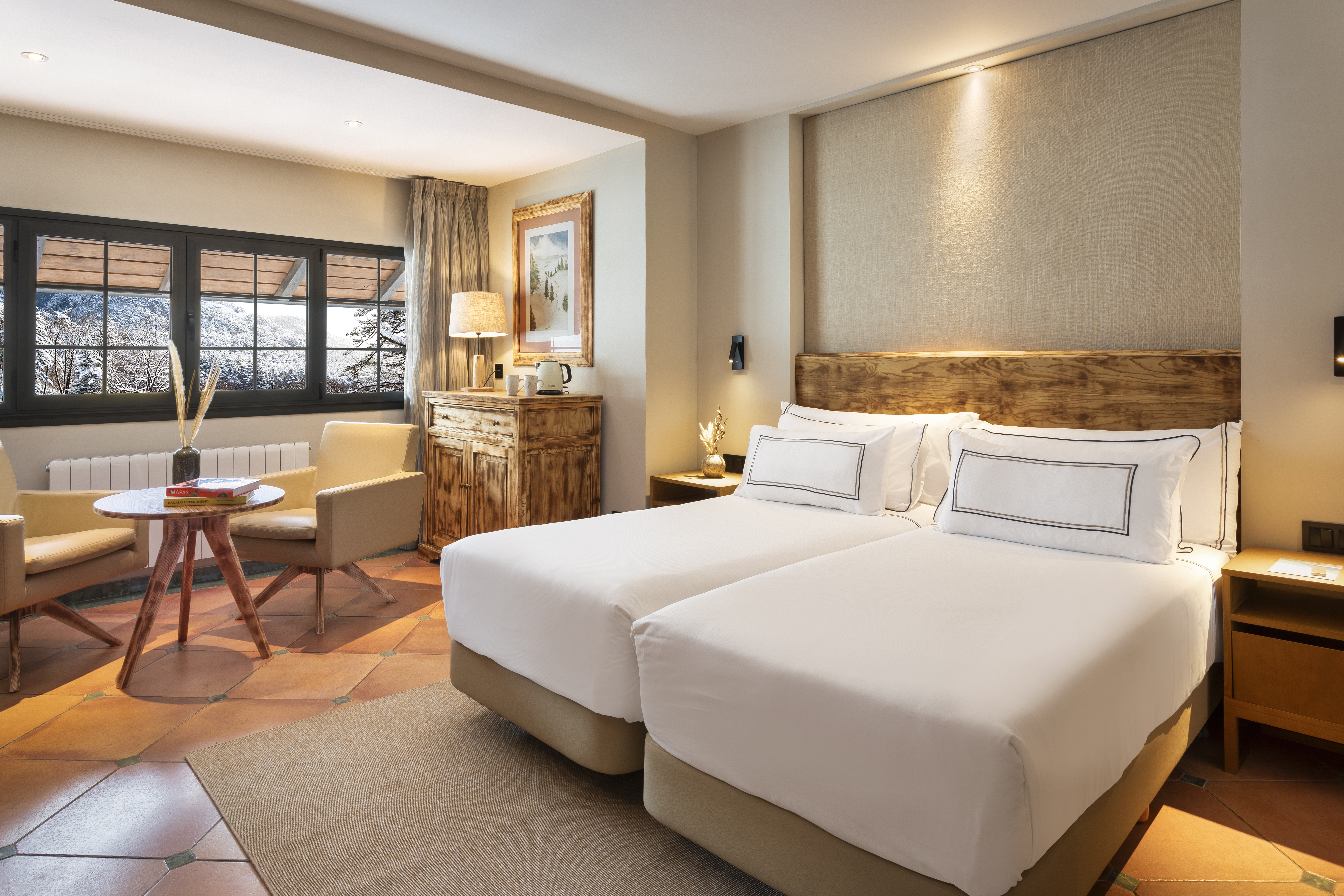 Cozy hotel bedroom with twin beds, sitting area, and snowy mountain view.