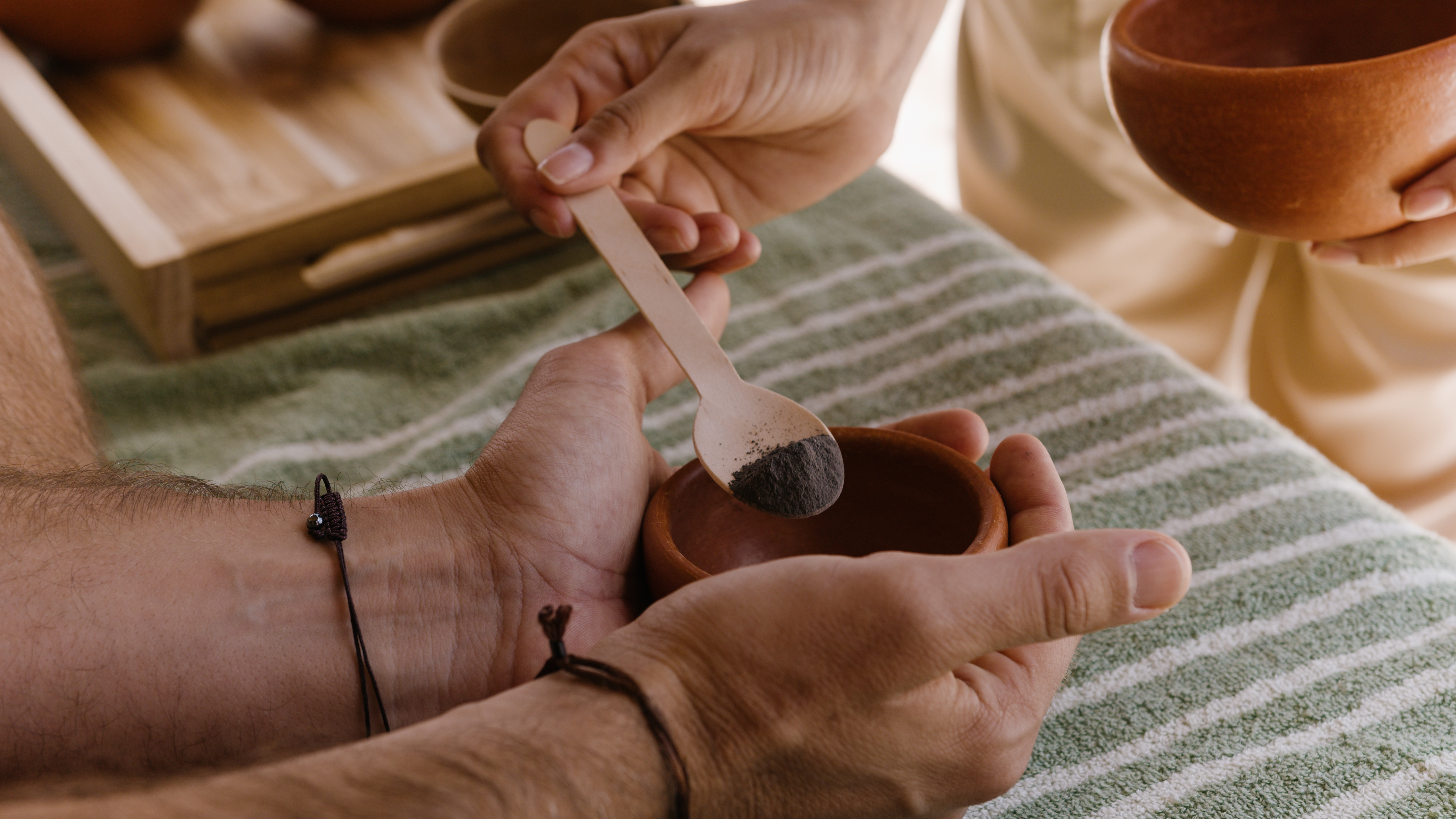 Hands preparing herbal powder in clay bowl with wooden spoon for wellness.