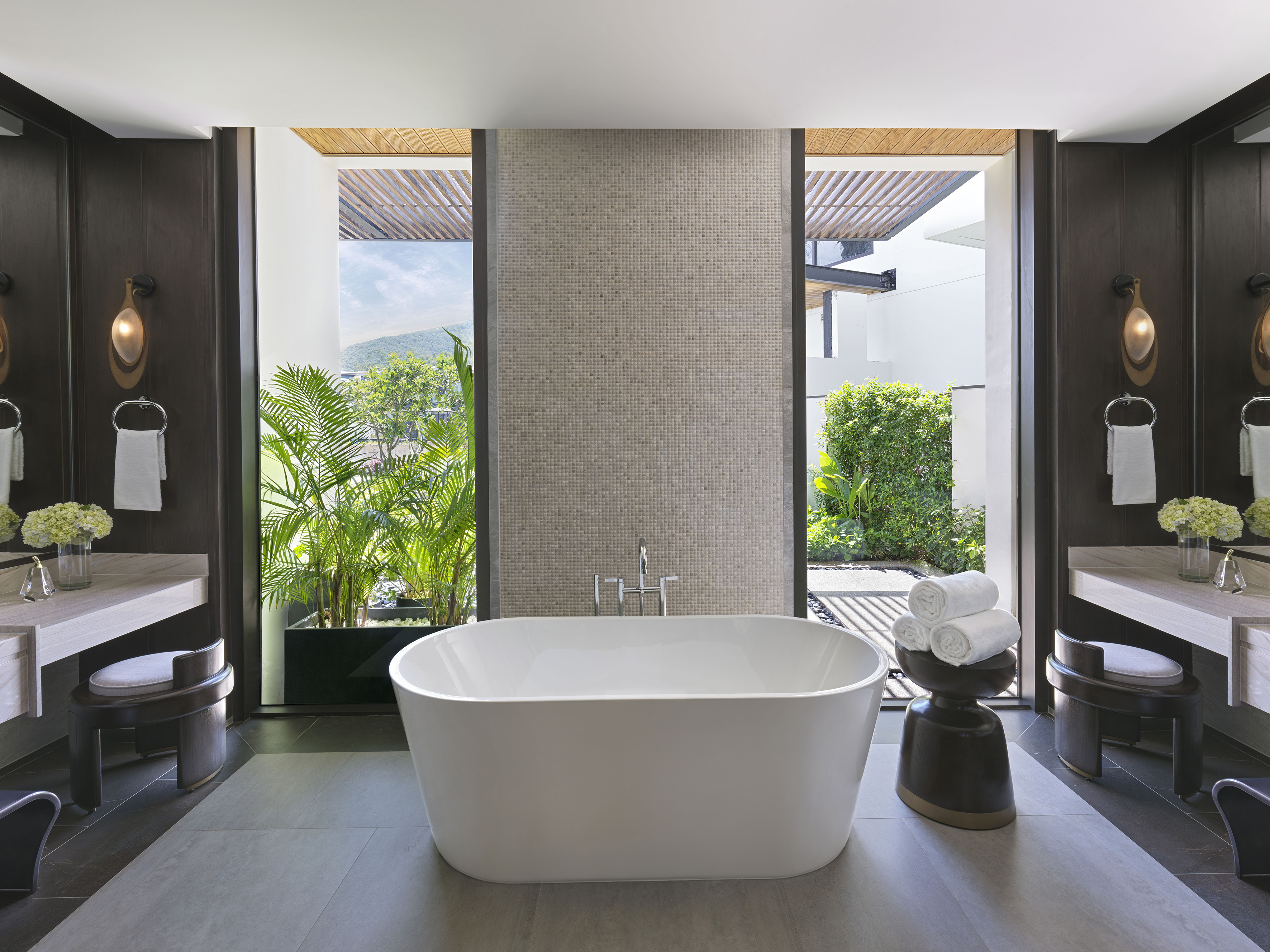 Modern luxury bathroom with freestanding tub, dual vanities, and tropical outdoor view.
