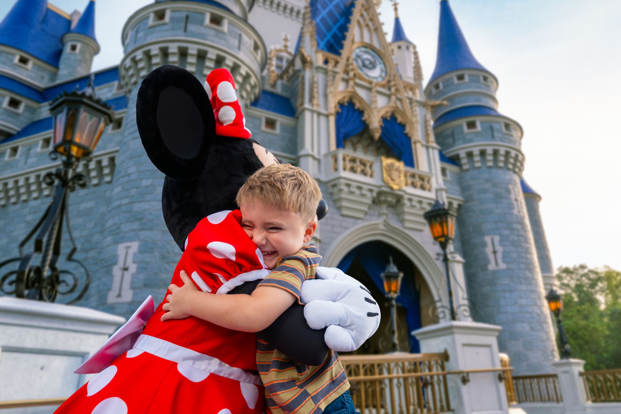 Happy boy hugging Minnie Mouse in front of Cinderella Castle at Disney World.