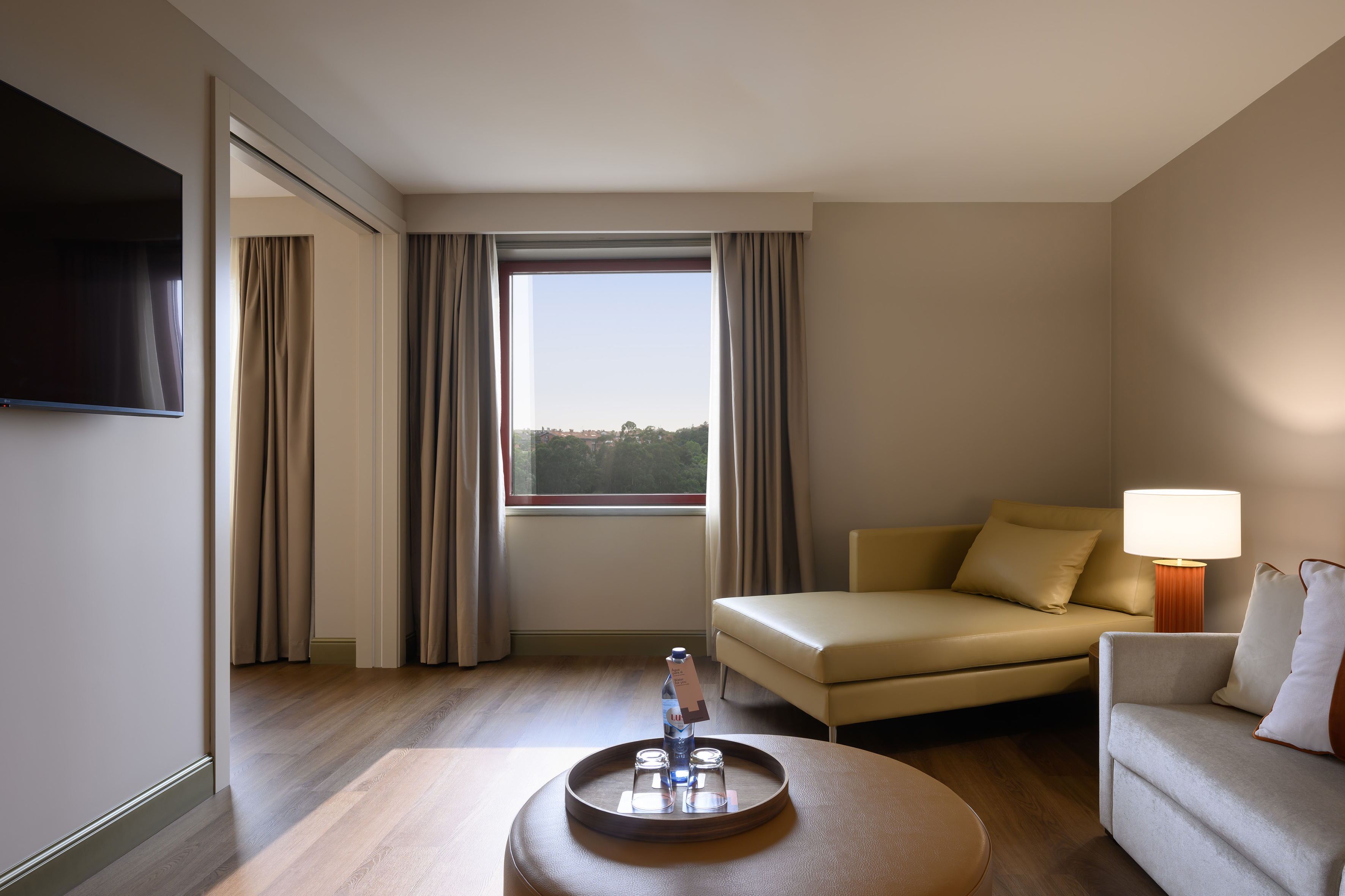 Modern hotel living area with chaise lounge, sofa, and scenic window view.