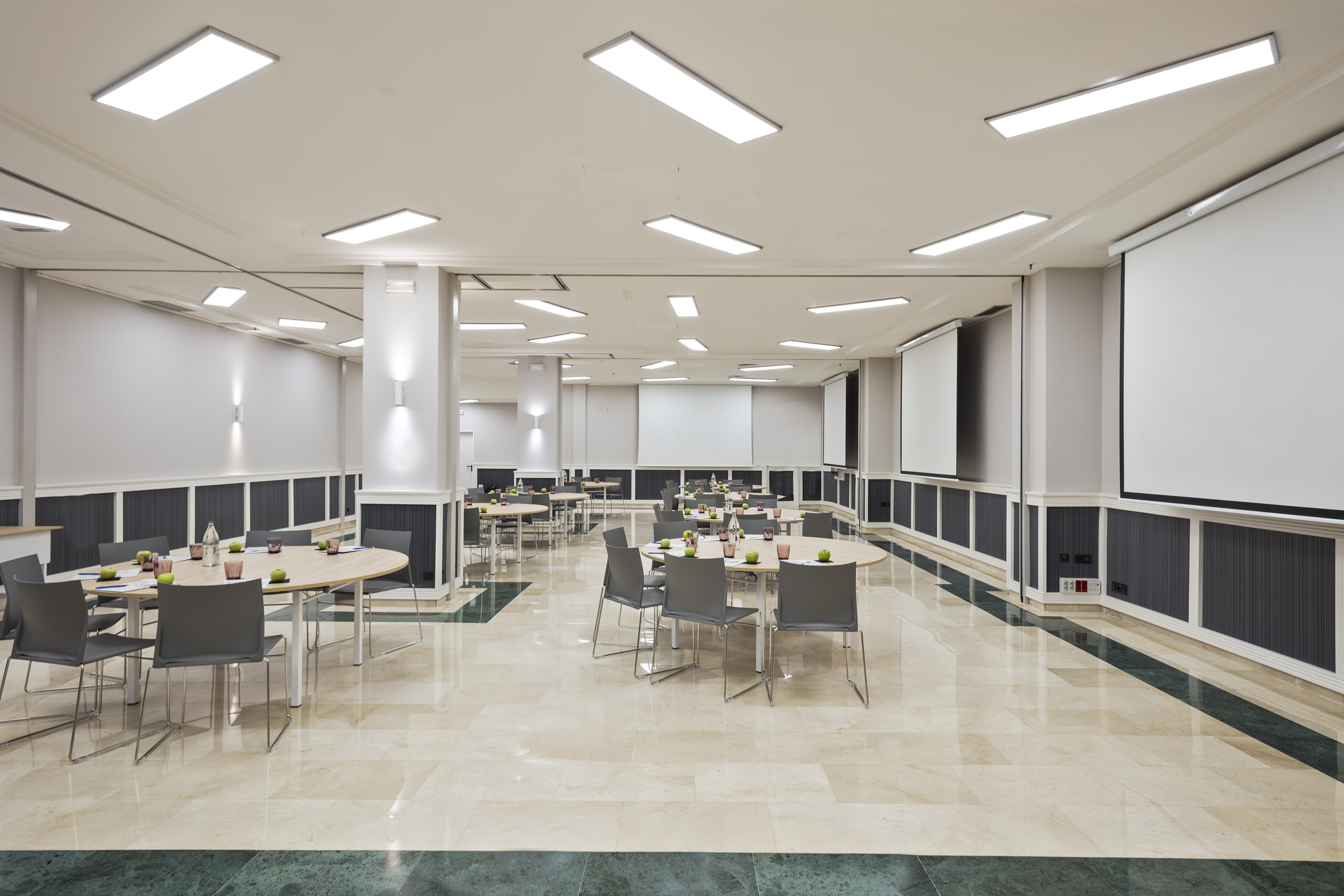 Modern conference room with tables, chairs, and multiple presentation screens.
