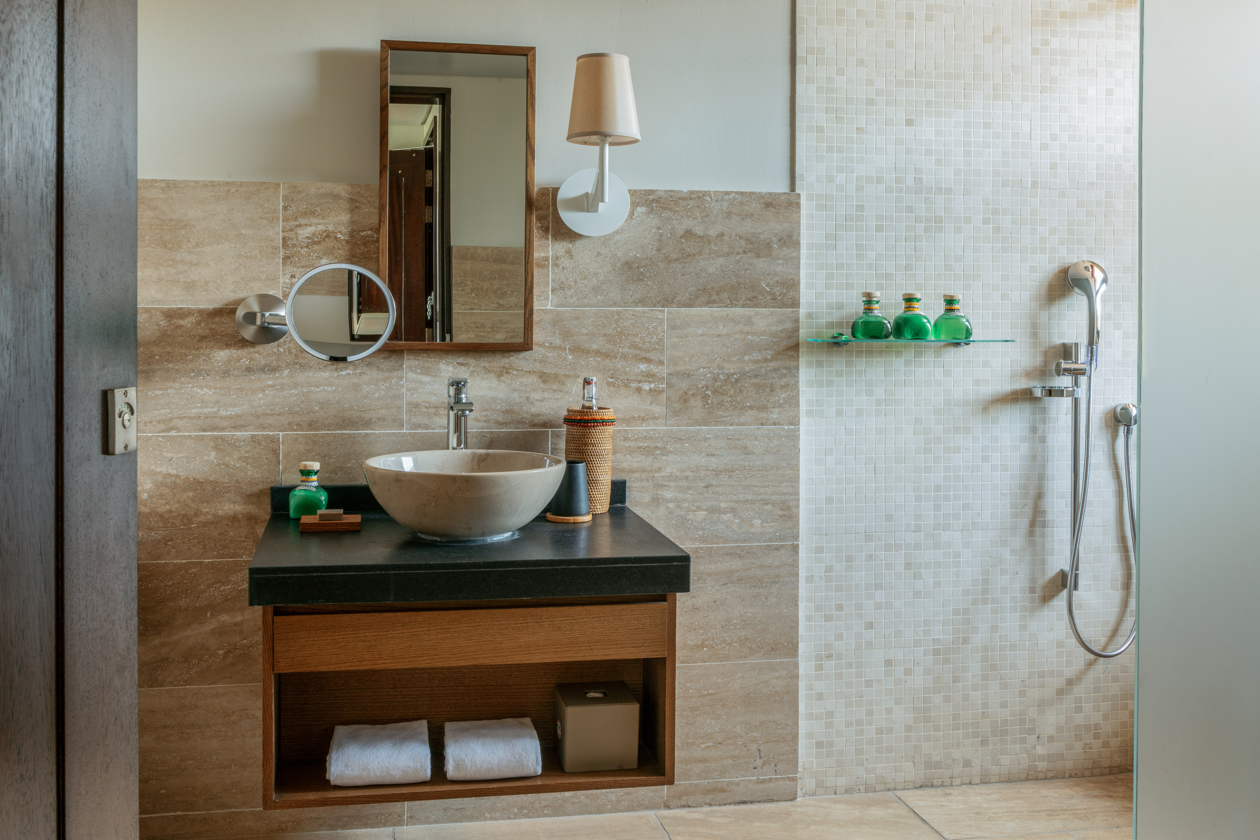 Spa bathroom with stone vessel sink, wooden vanity, marble tile, and shower.
