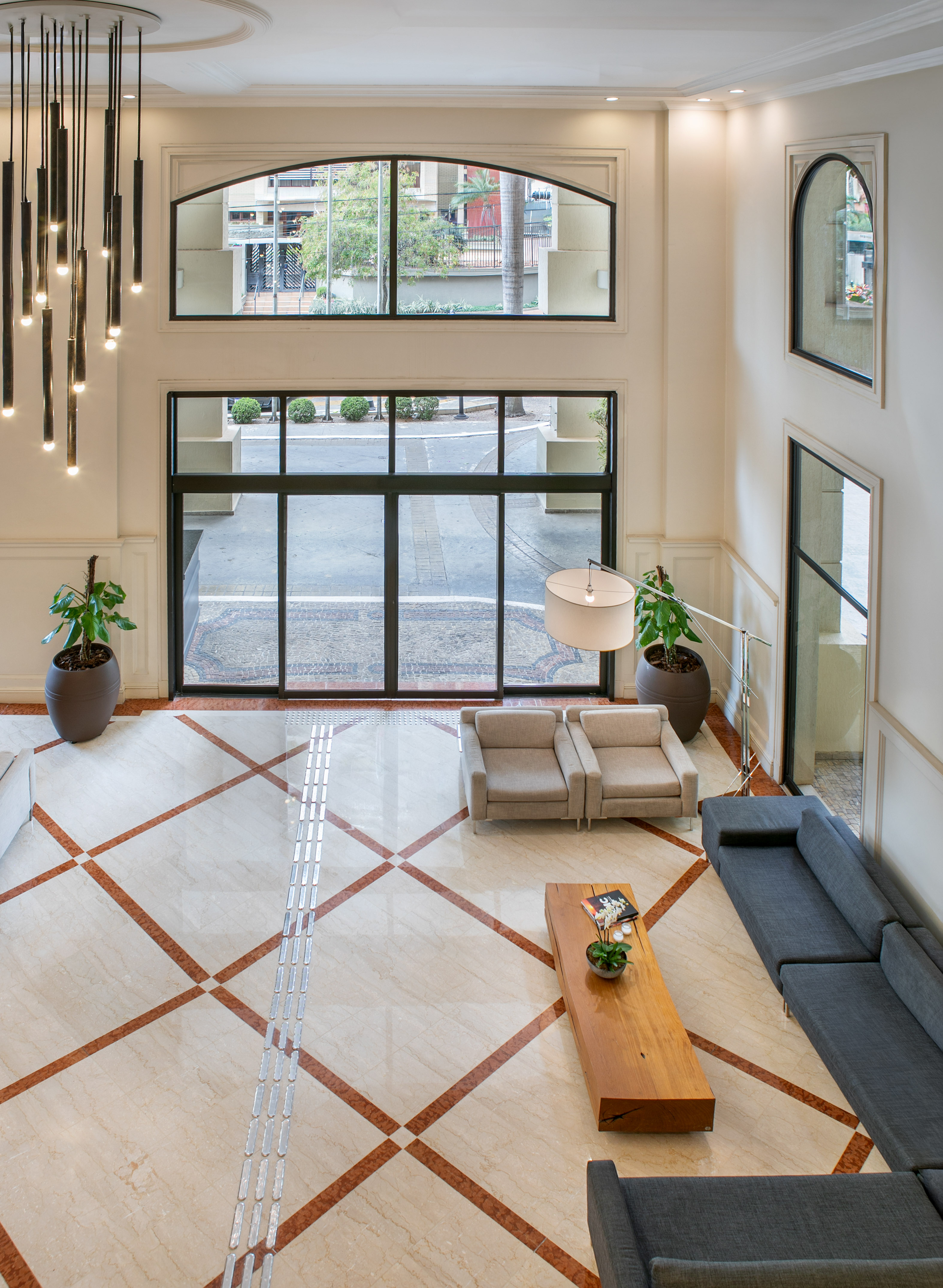 Modern high-ceiling lobby with marble floor, glass entrance, grey sofas, and chandelier. - Meliá Campinas, Campinas