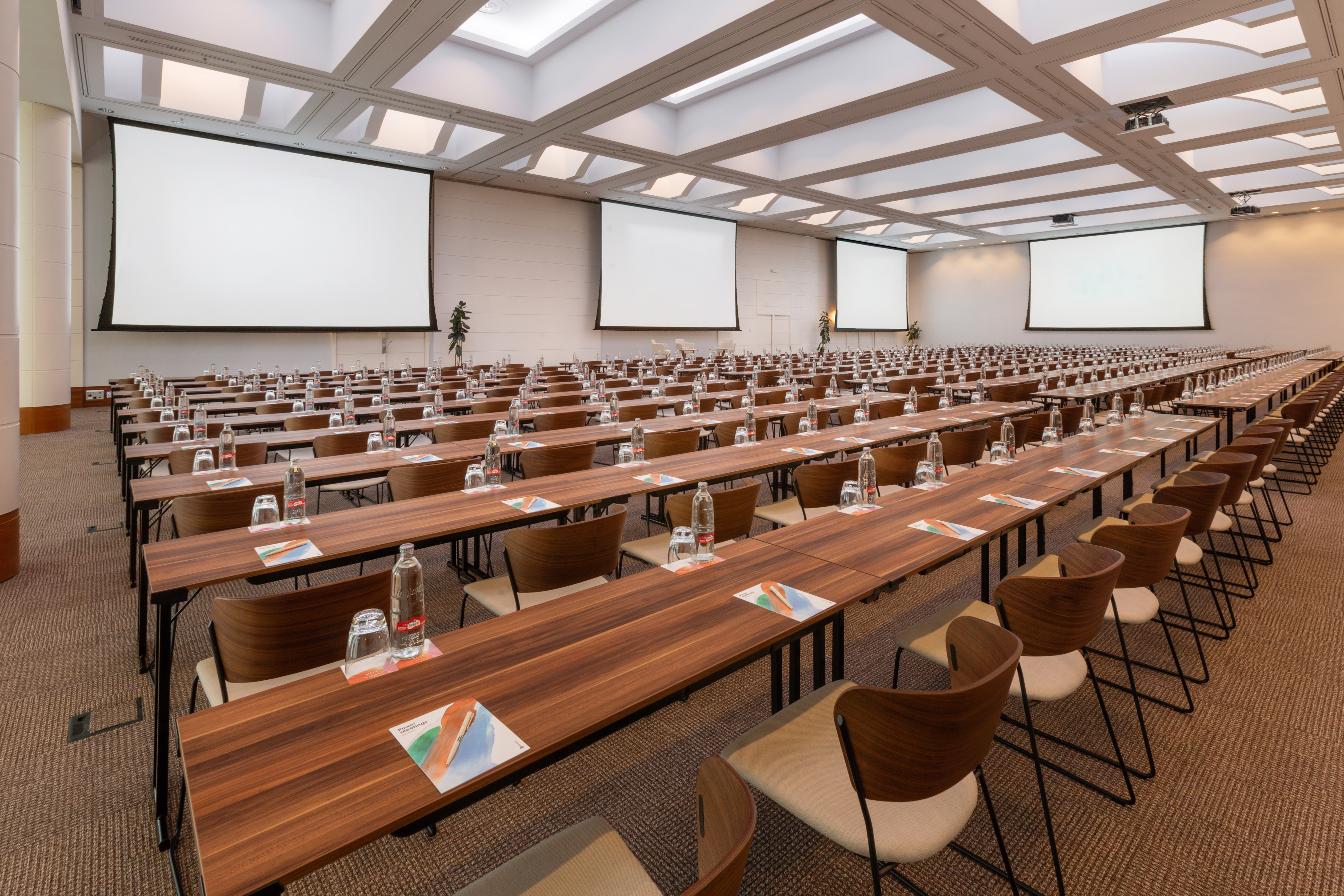 Hotel conference room with rows of tables, chairs, and multiple projection screens.