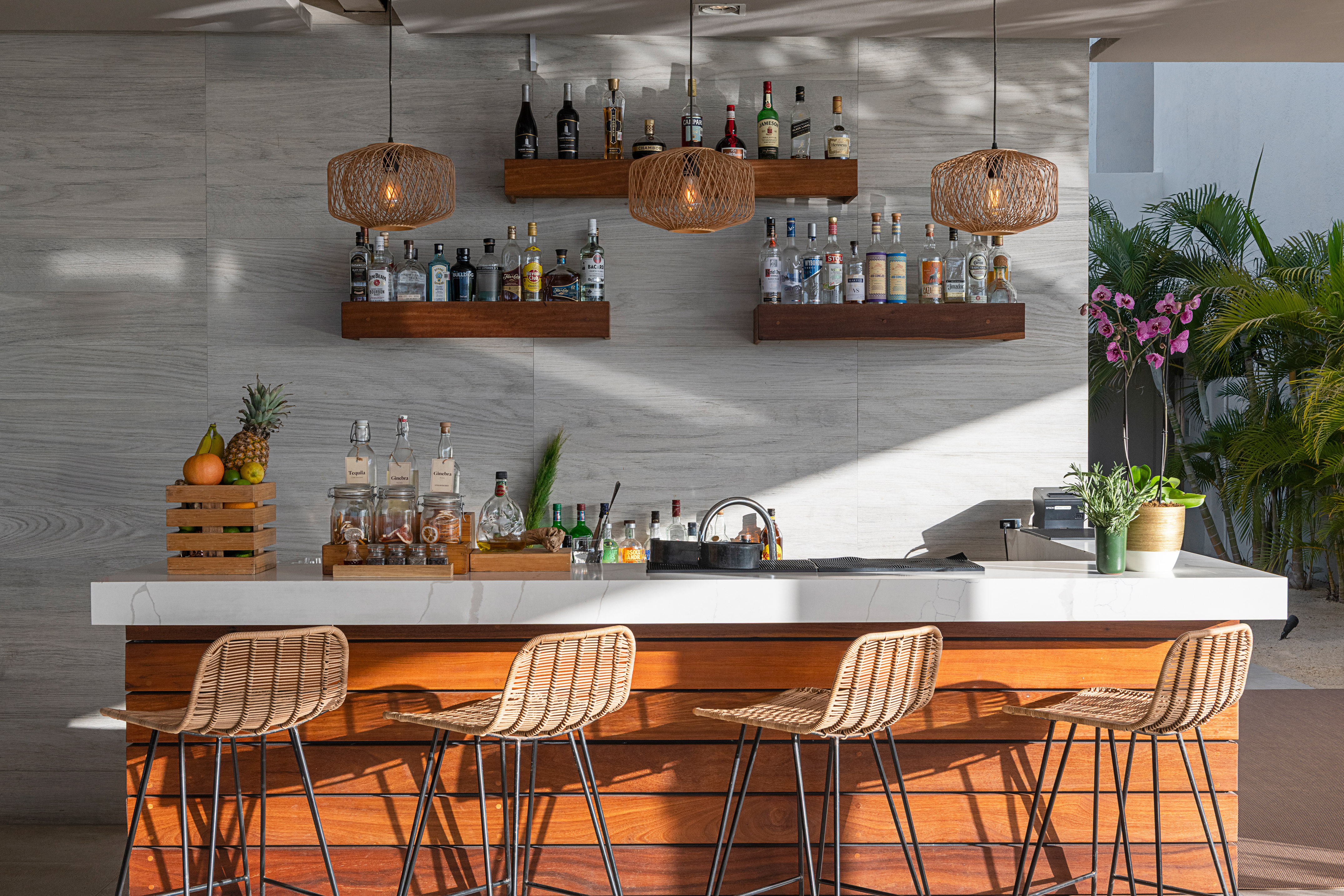 Outdoor resort bar with wicker stools, liquor bottles, and modern lighting.