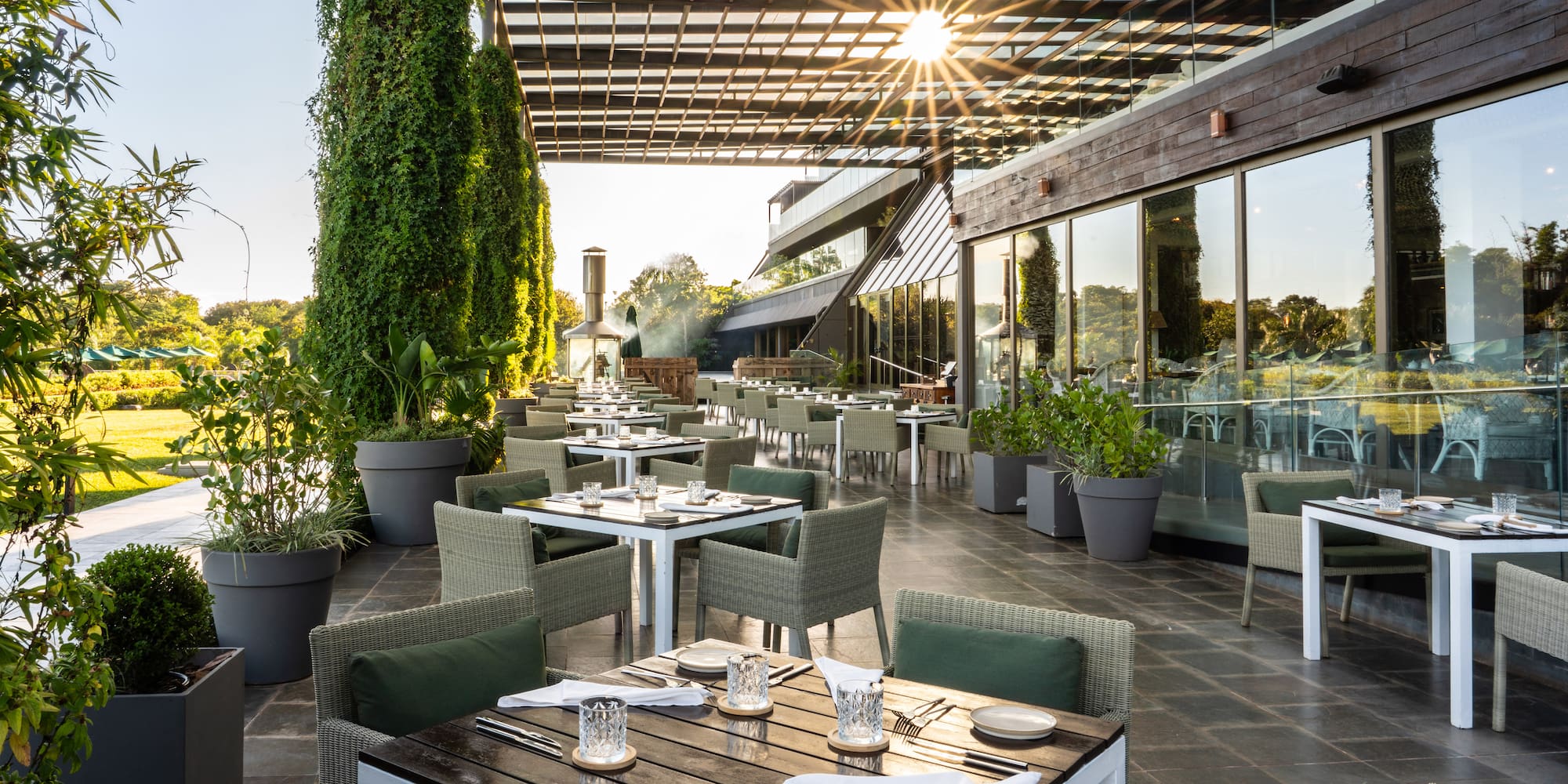 Modern outdoor restaurant patio with set tables, green seating, and lush garden.