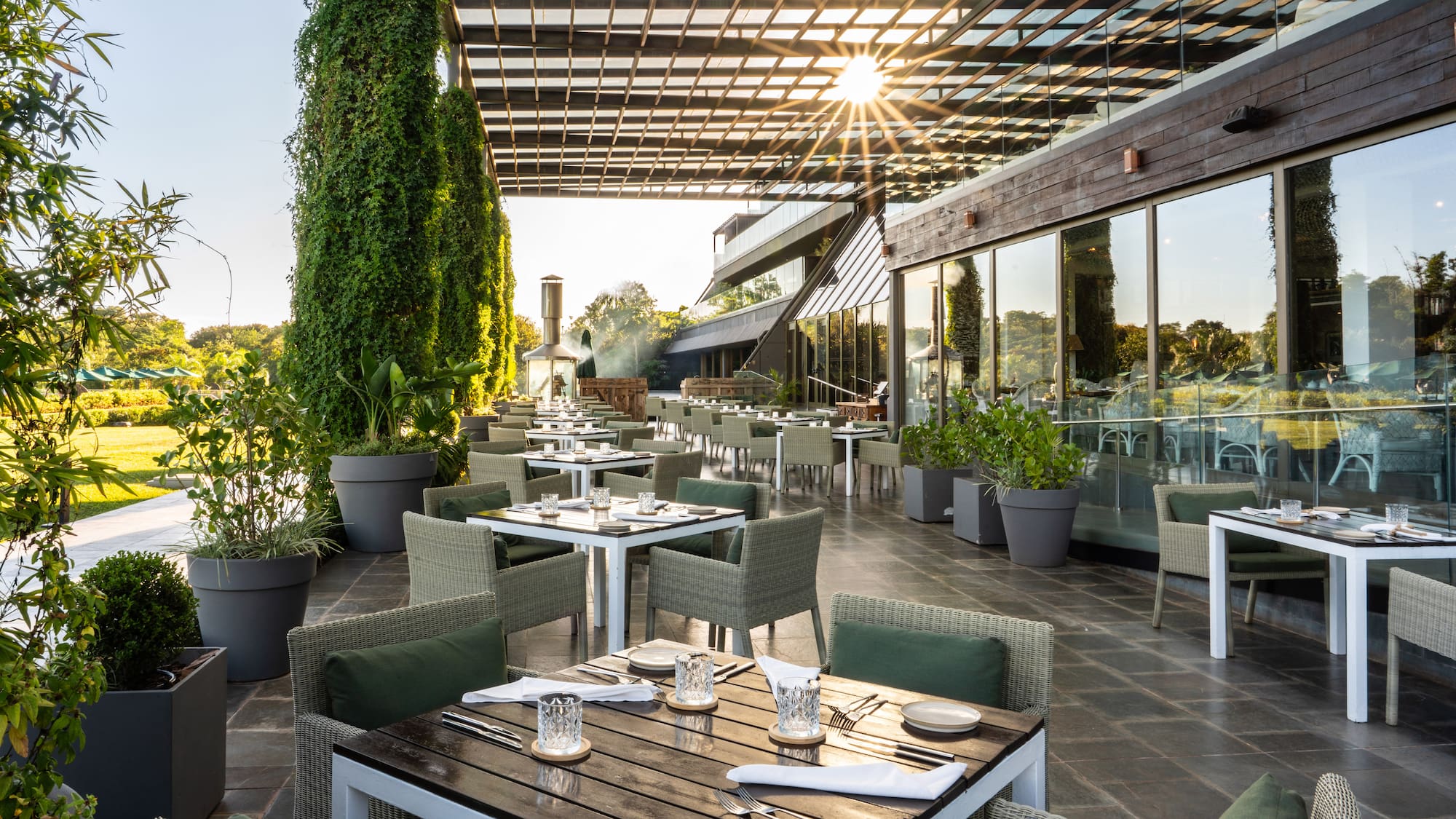 Modern outdoor restaurant patio with set tables, green seating, and lush garden.