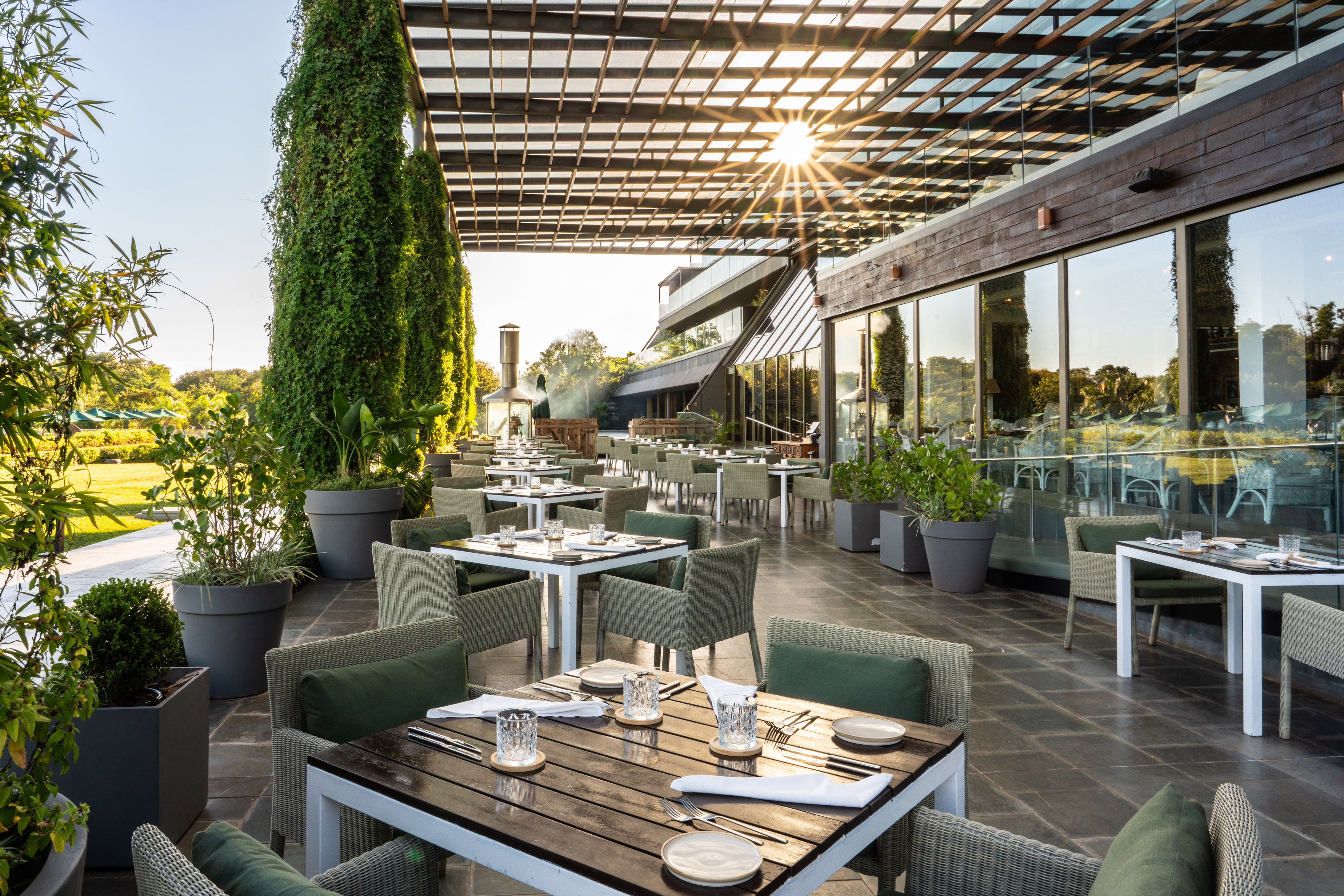 Modern outdoor restaurant patio with set tables, green seating, and lush garden.