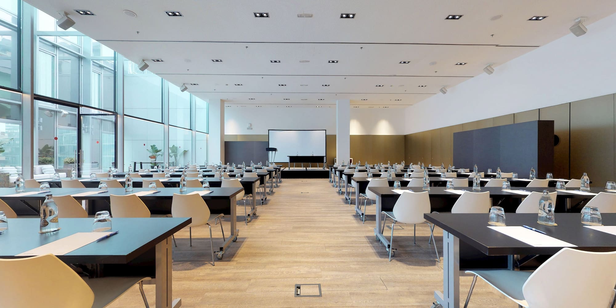 Modern conference room with classroom setup, projection screen, and large windows.