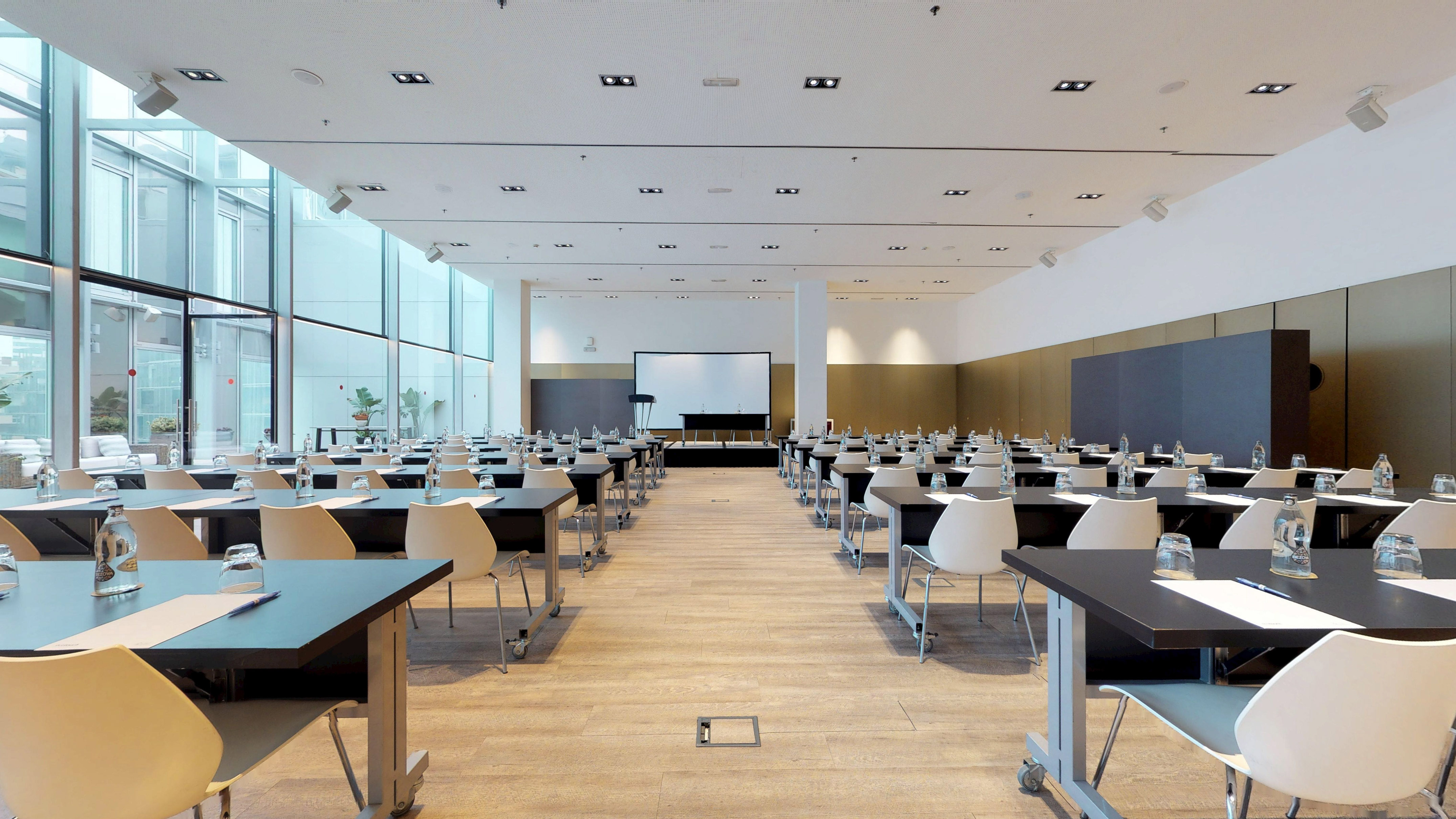 Modern conference room with classroom setup, projection screen, and large windows.