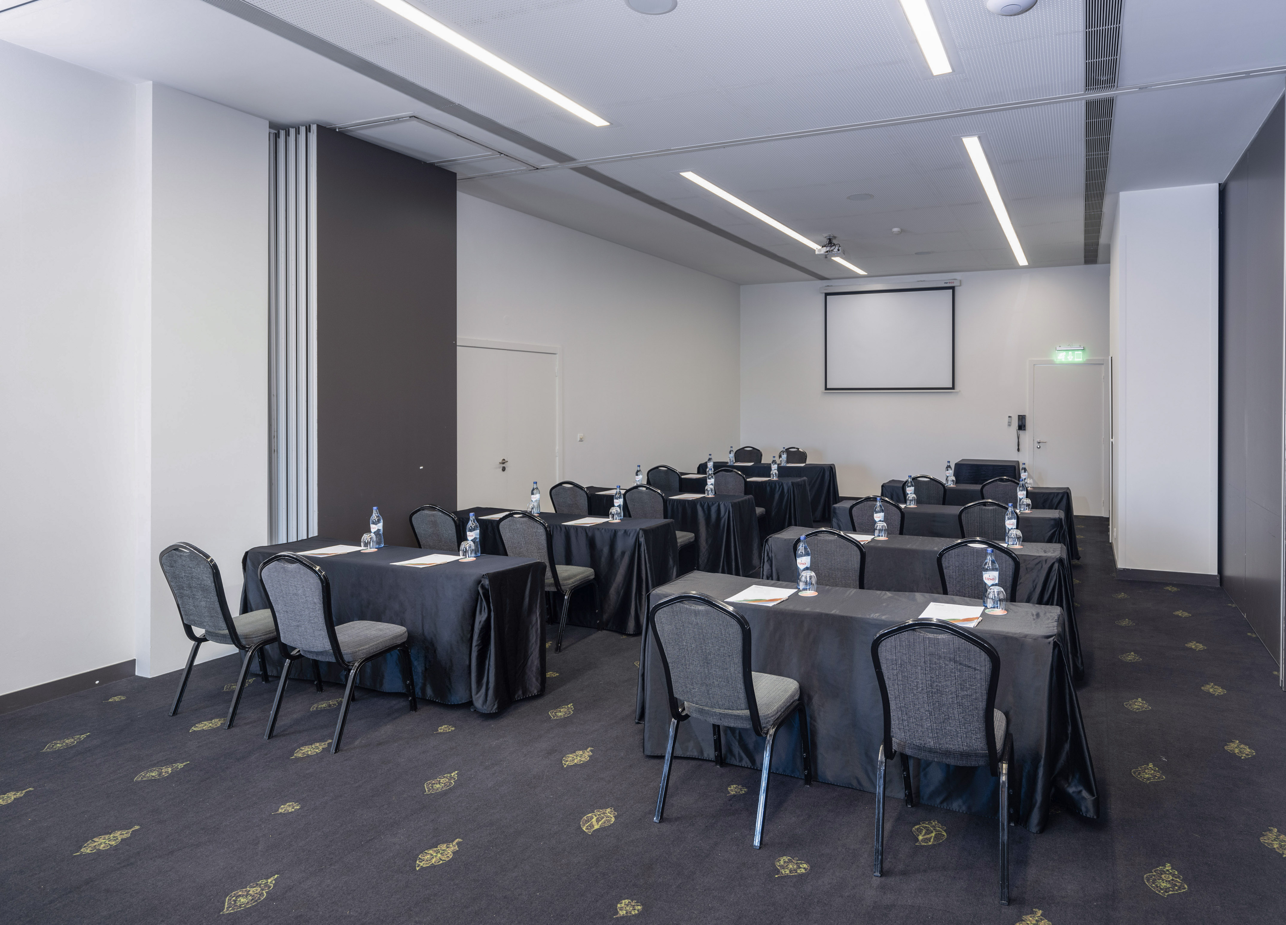 Empty conference room: rows of tables, chairs, projector screen.