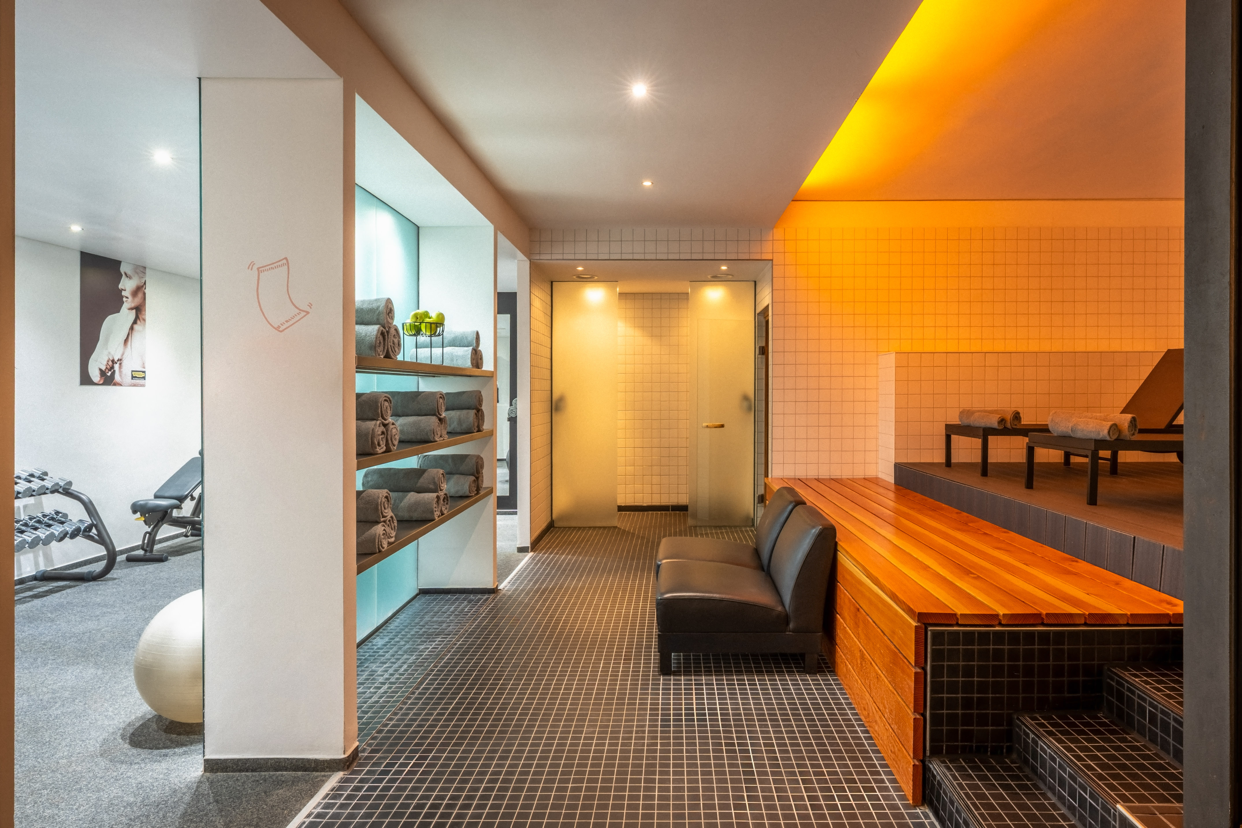 Modern spa wellness area with towel shelves, tiled floor, lounge, sauna, and gym.