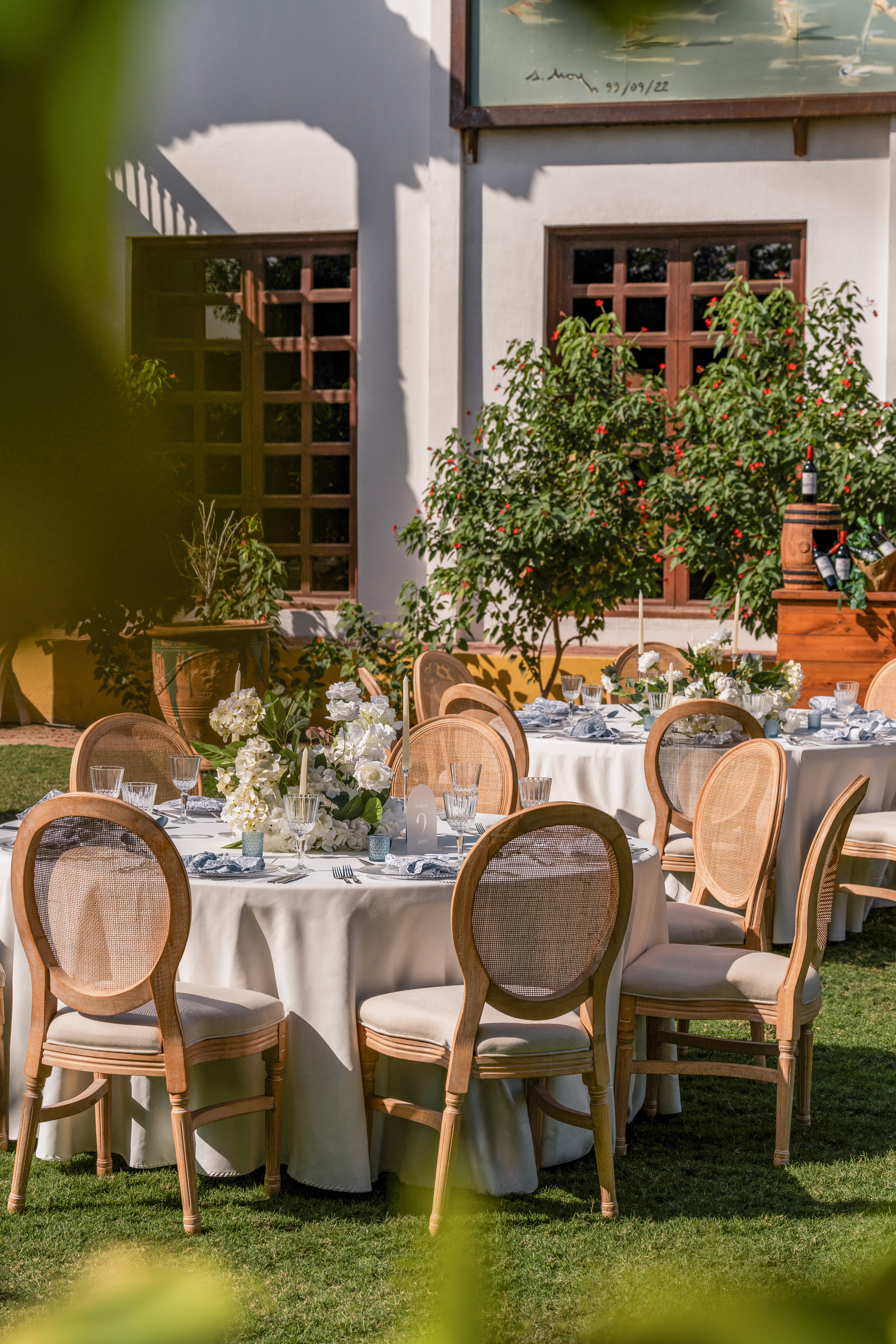Elegant outdoor reception tables with white flowers and natural cane chairs.