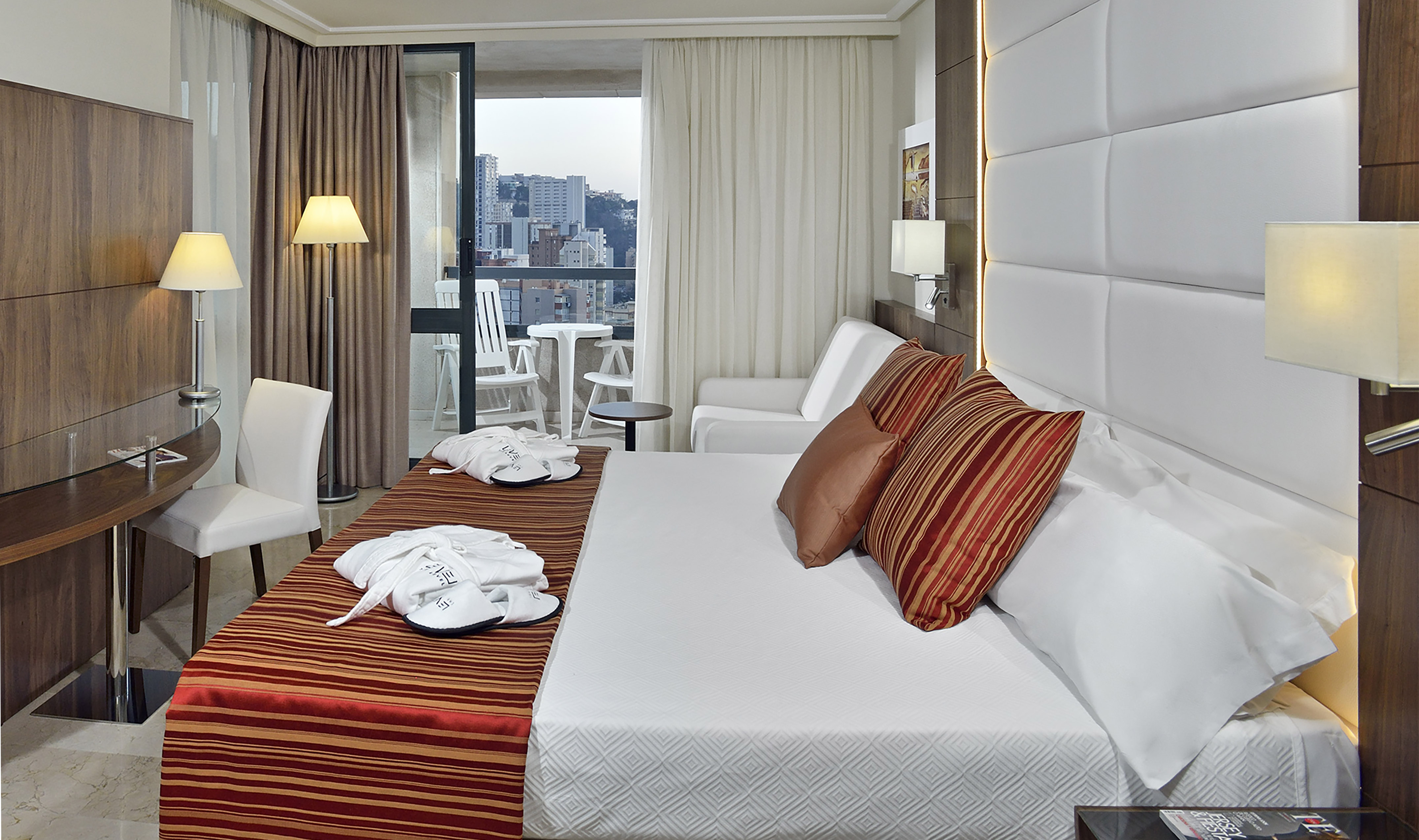 Comfortable hotel room with king bed, city view balcony, desk, and robes.