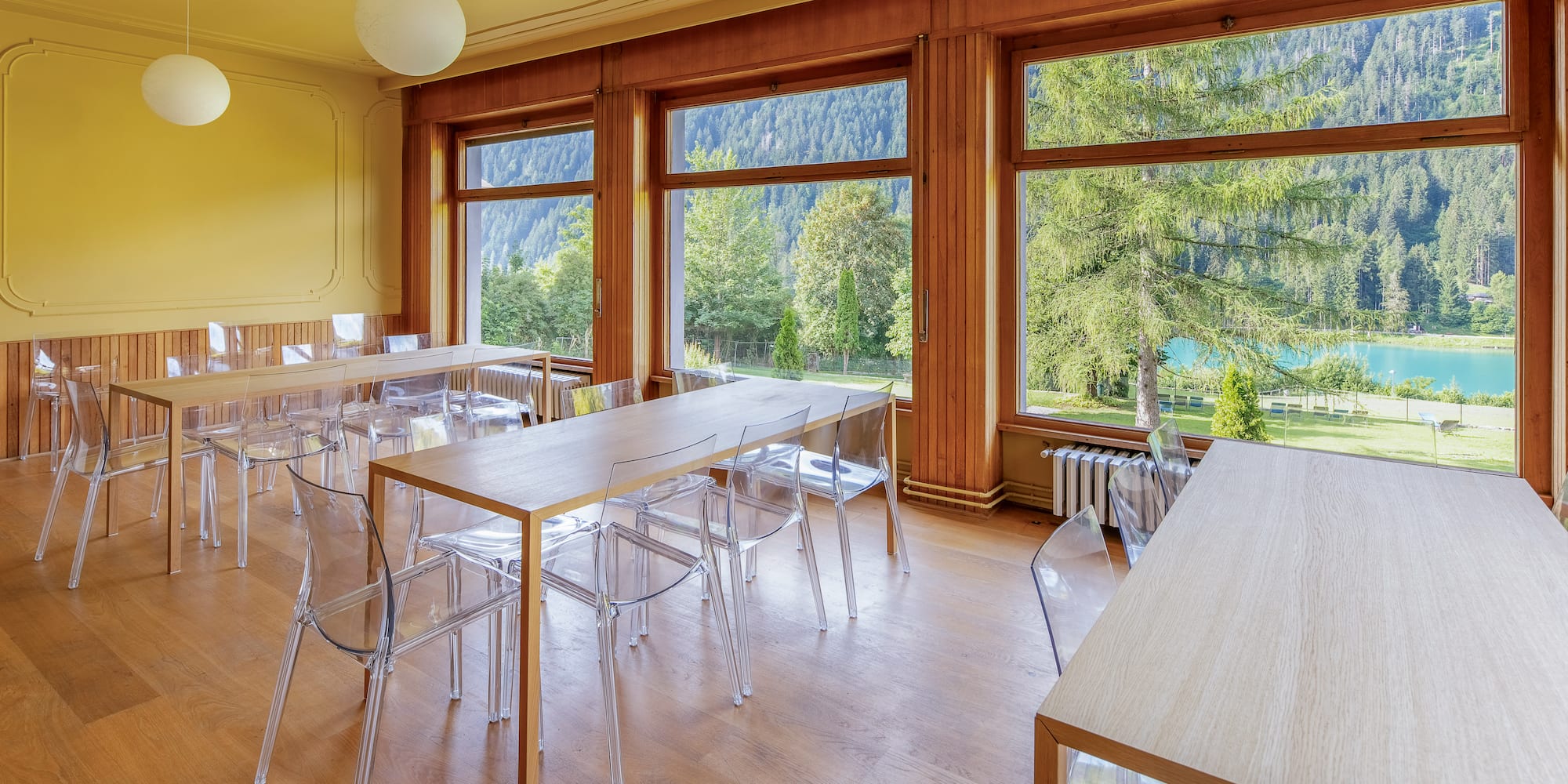 Dining room with wooden tables, clear chairs, and panoramic lake & mountain views.