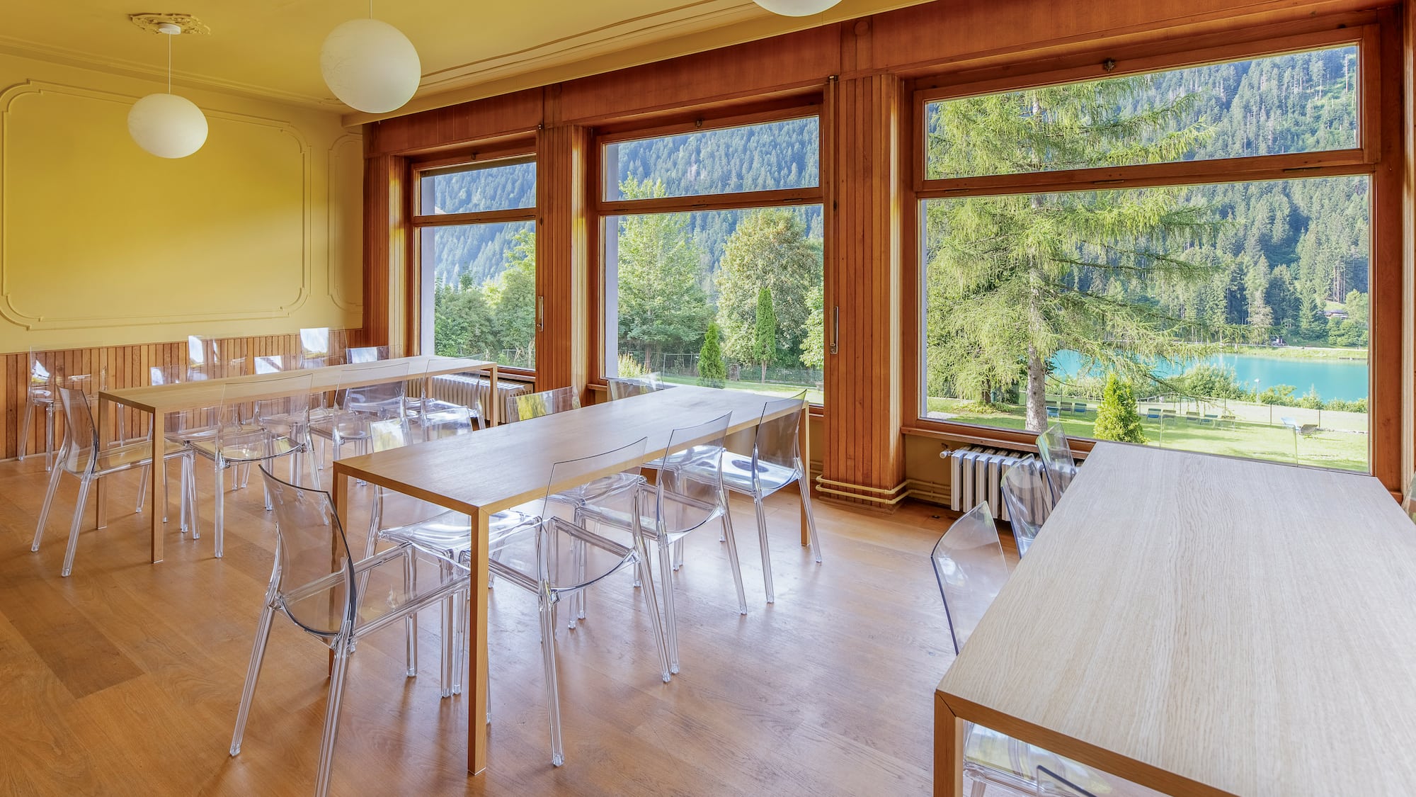 Dining room with wooden tables, clear chairs, and panoramic lake & mountain views.