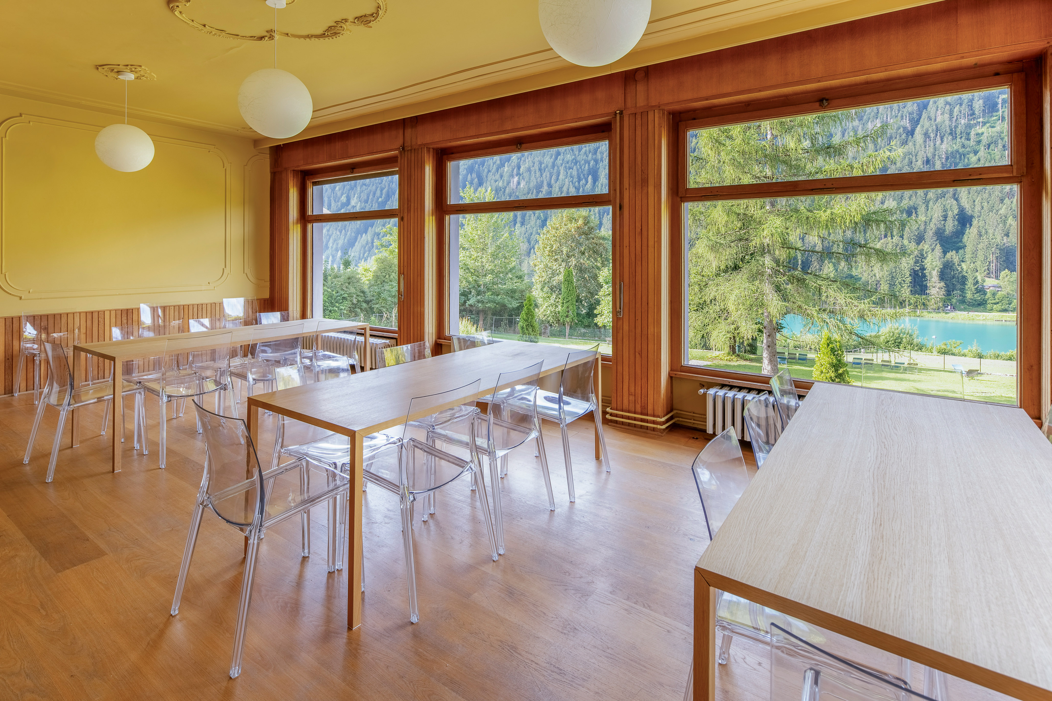 Dining room with wooden tables, clear chairs, and panoramic lake & mountain views.