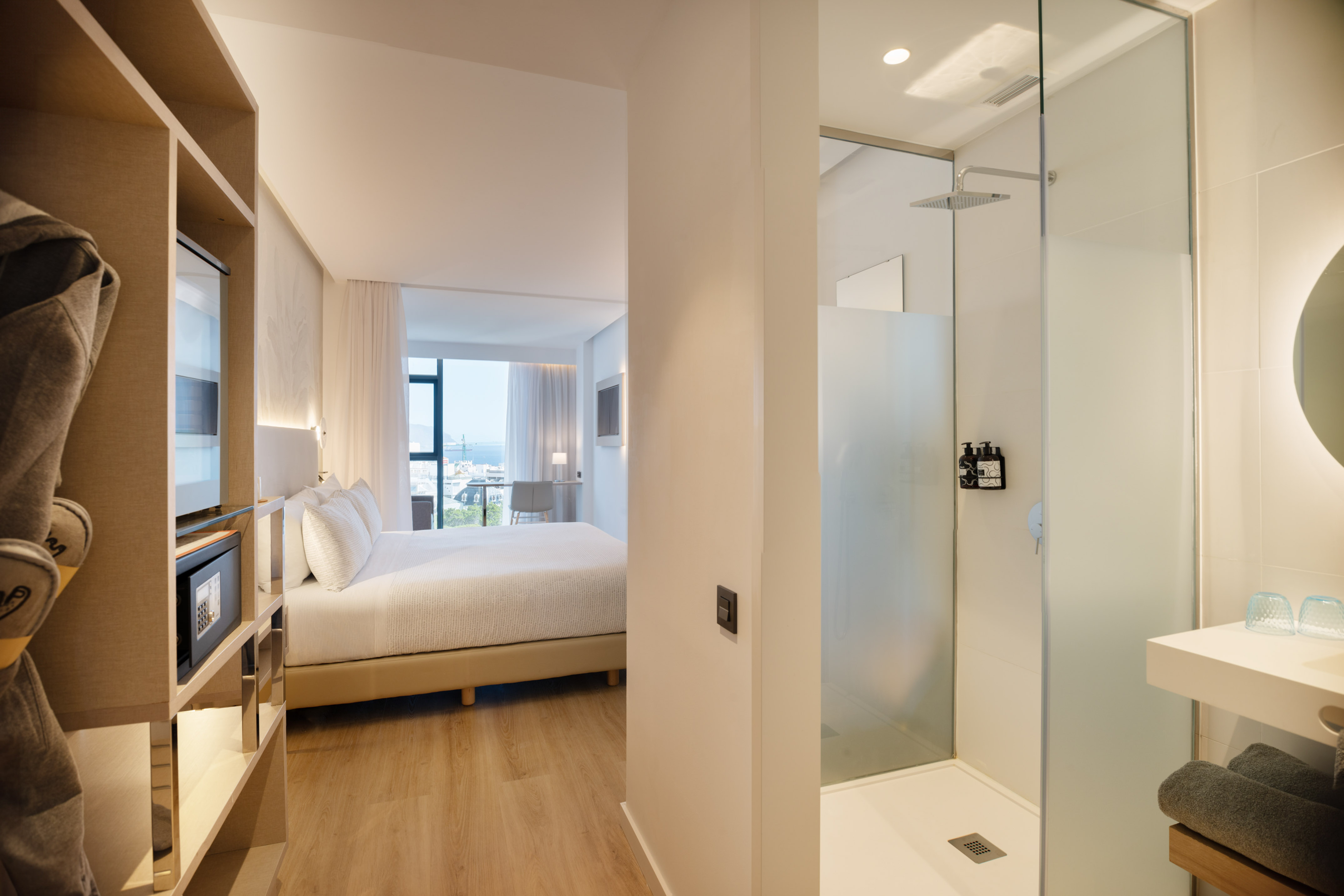 Contemporary hotel suite with bedroom, walk-in shower, and scenic ocean view.