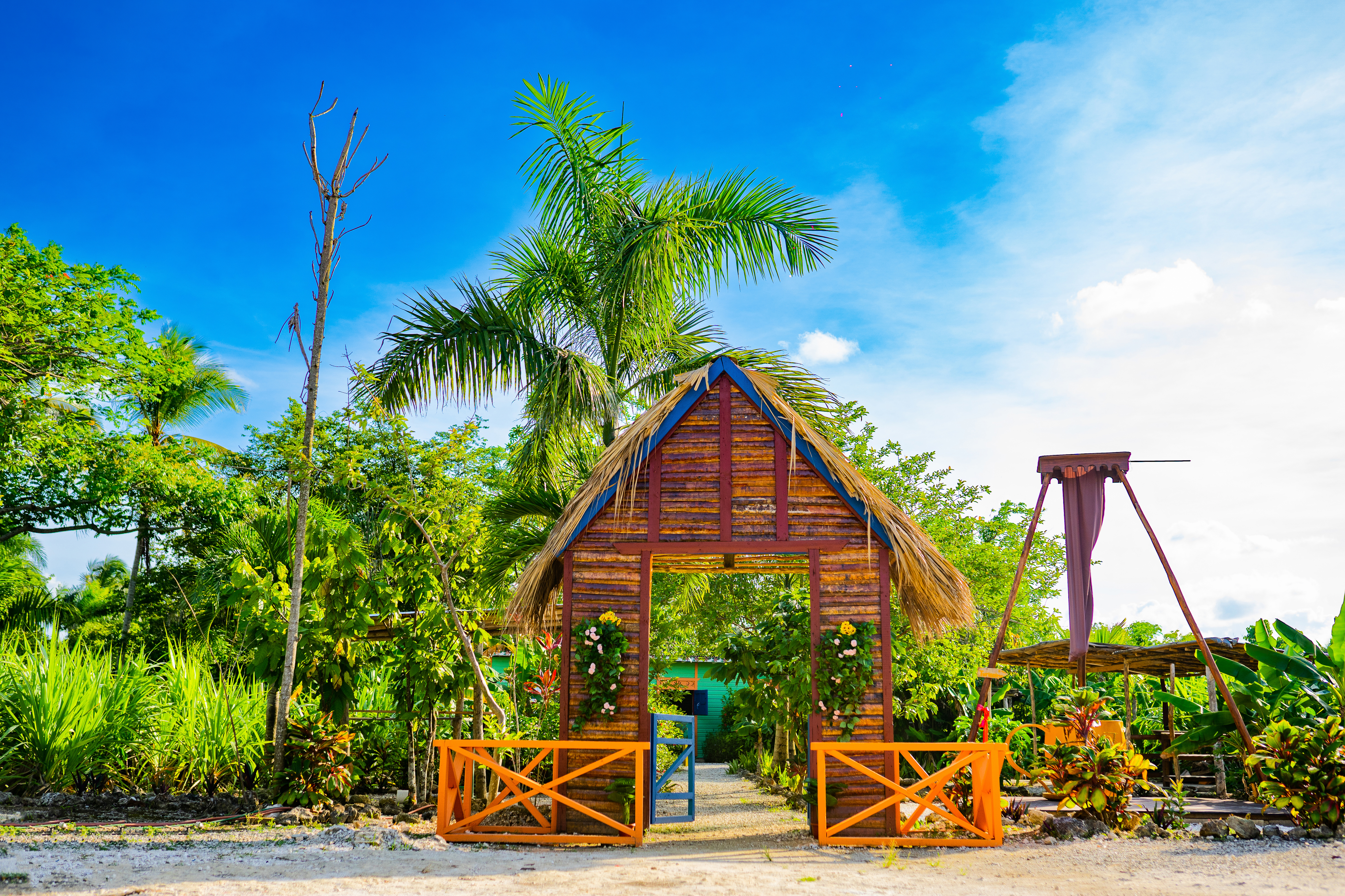 Wooden archway with thatched roof, orange gates, and tropical garden plants.