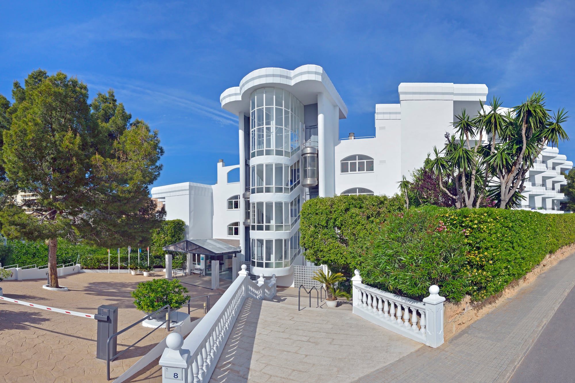 White modern hotel with curved glass spiral elevator and tropical landscaping.