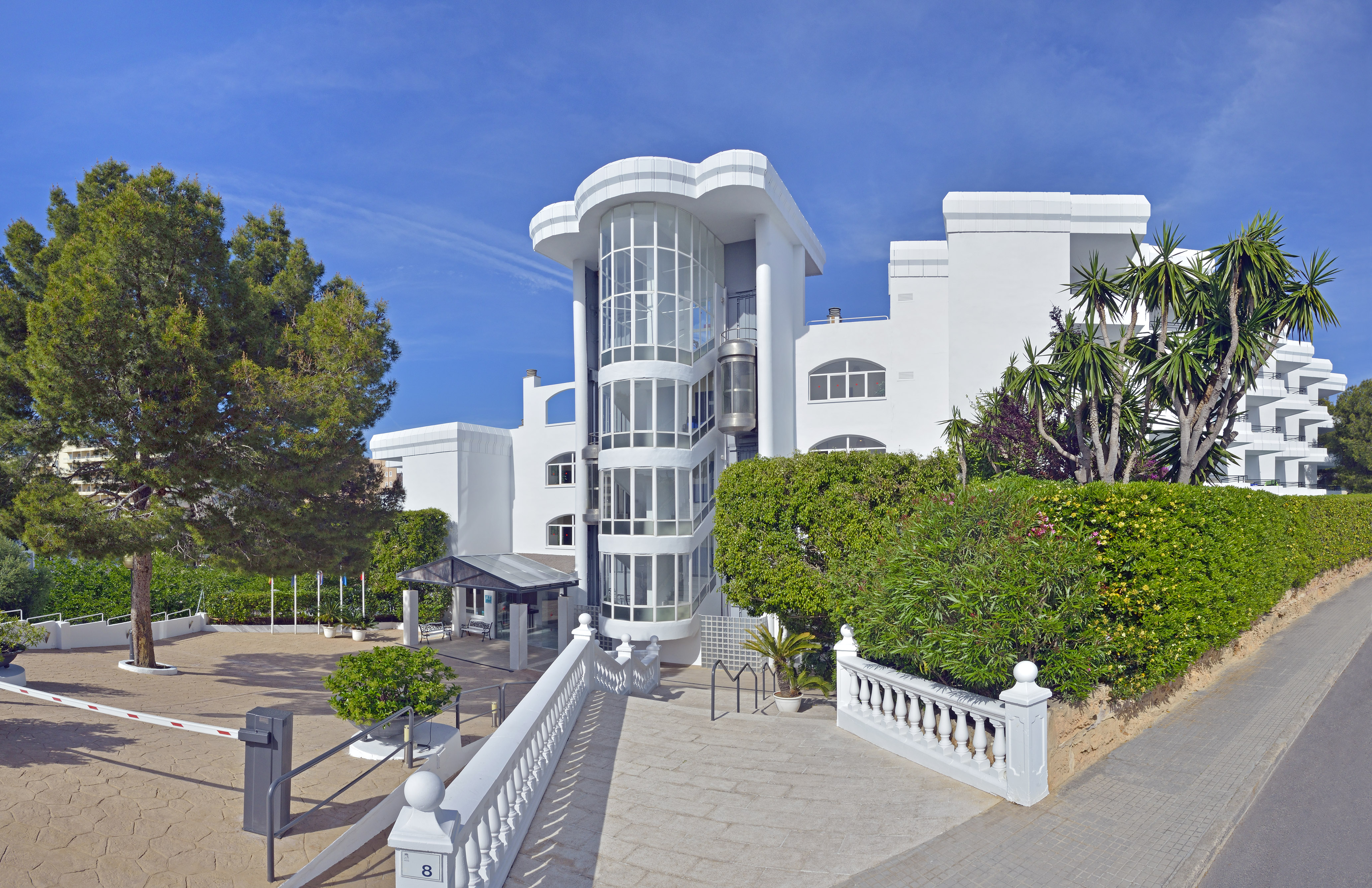 White modern hotel with curved glass spiral elevator and tropical landscaping.