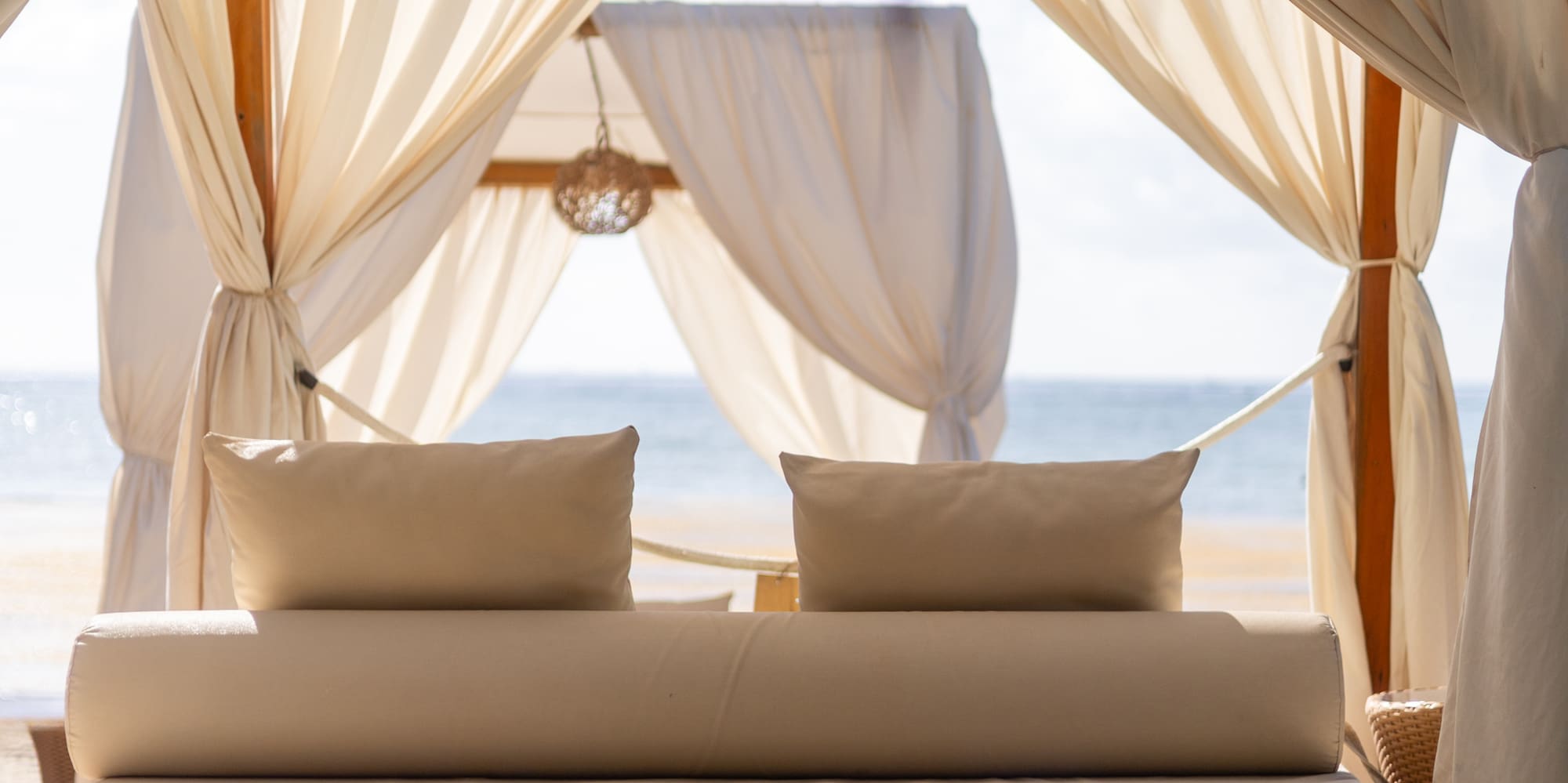White beach cabana with daybed on sand by the sea.