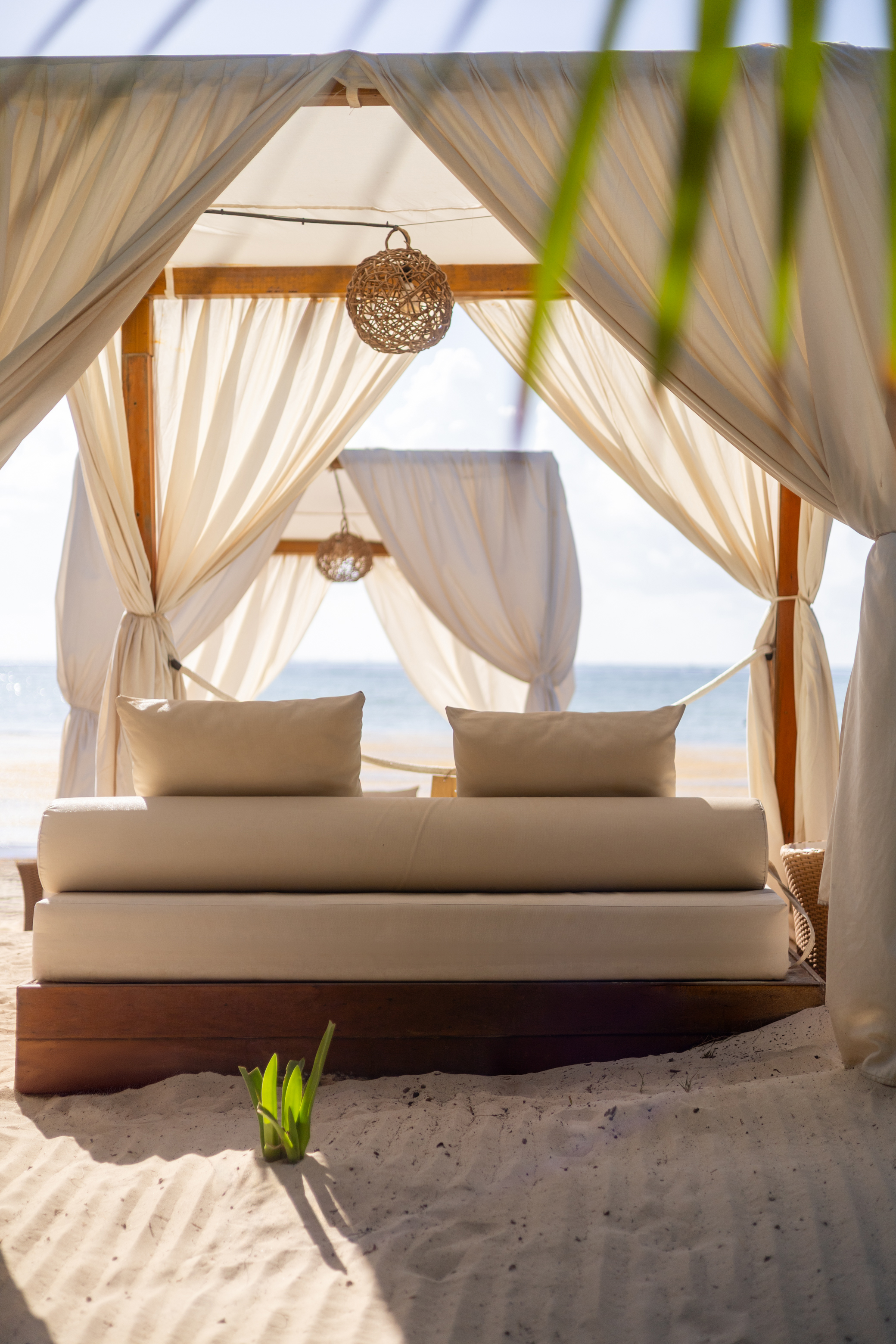 White beach cabana with daybed on sand by the sea.