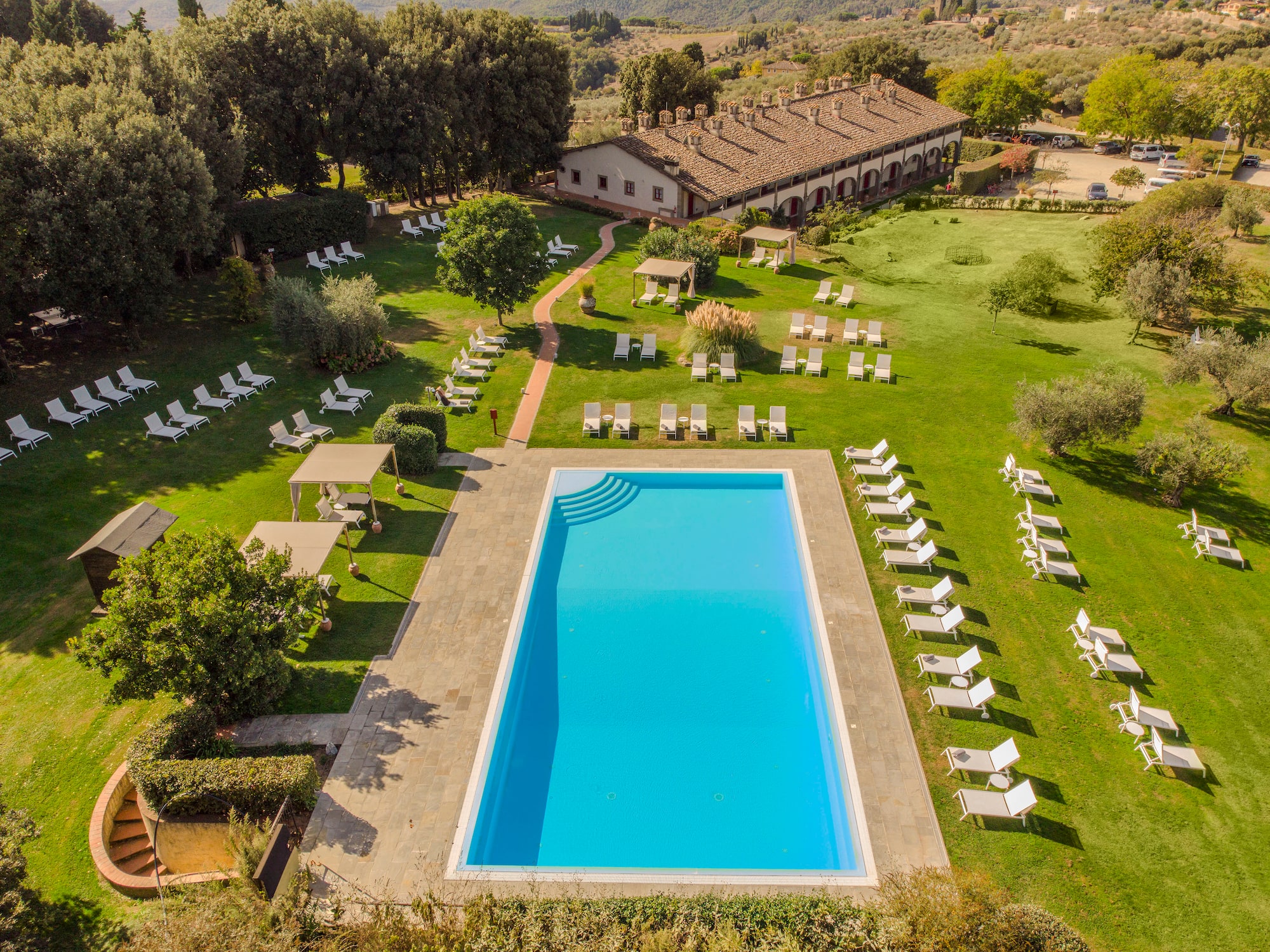 Large resort pool, many sun loungers, and traditional villa on green grounds.