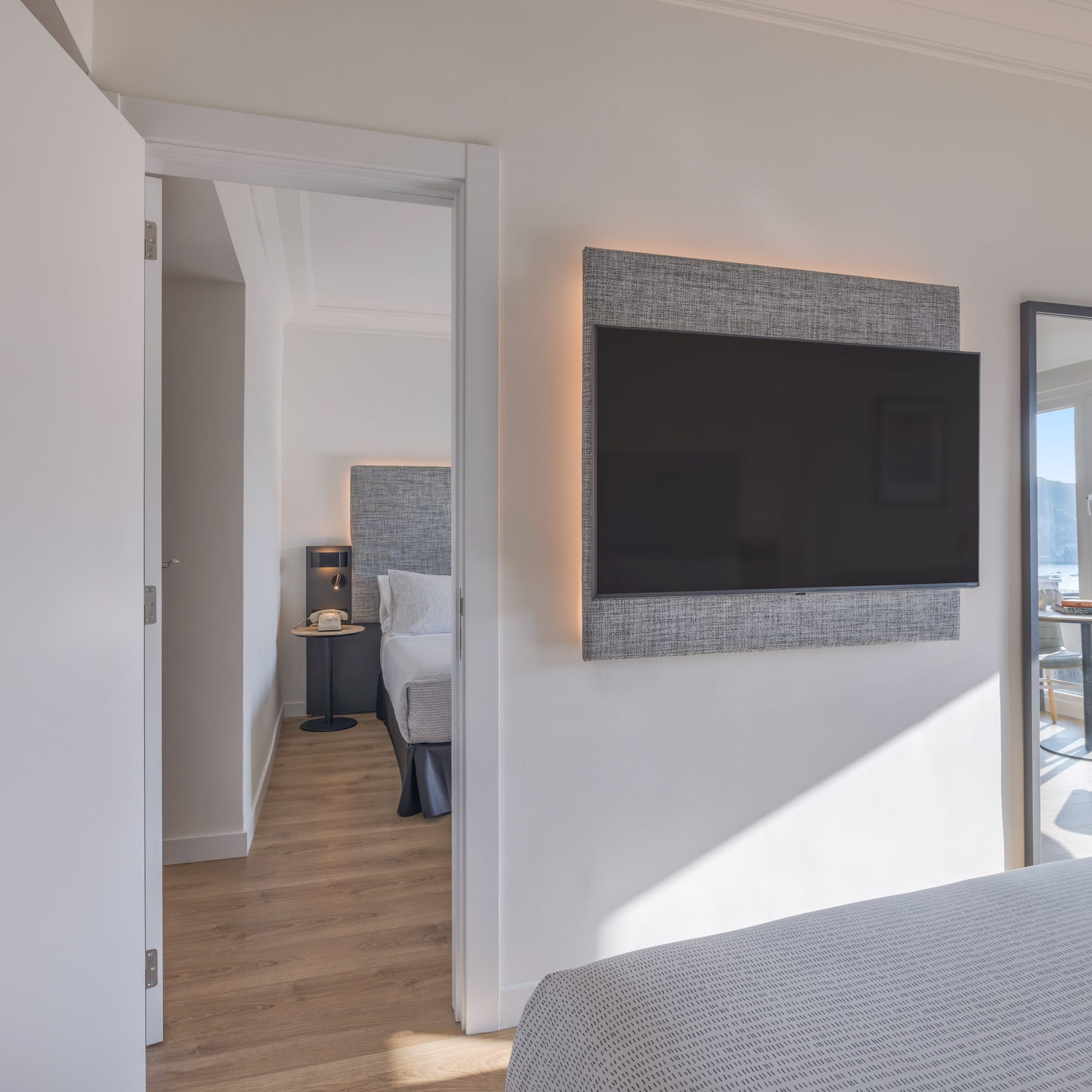 Habitación de hotel moderna con TV, cama y vista al mar reflejada.